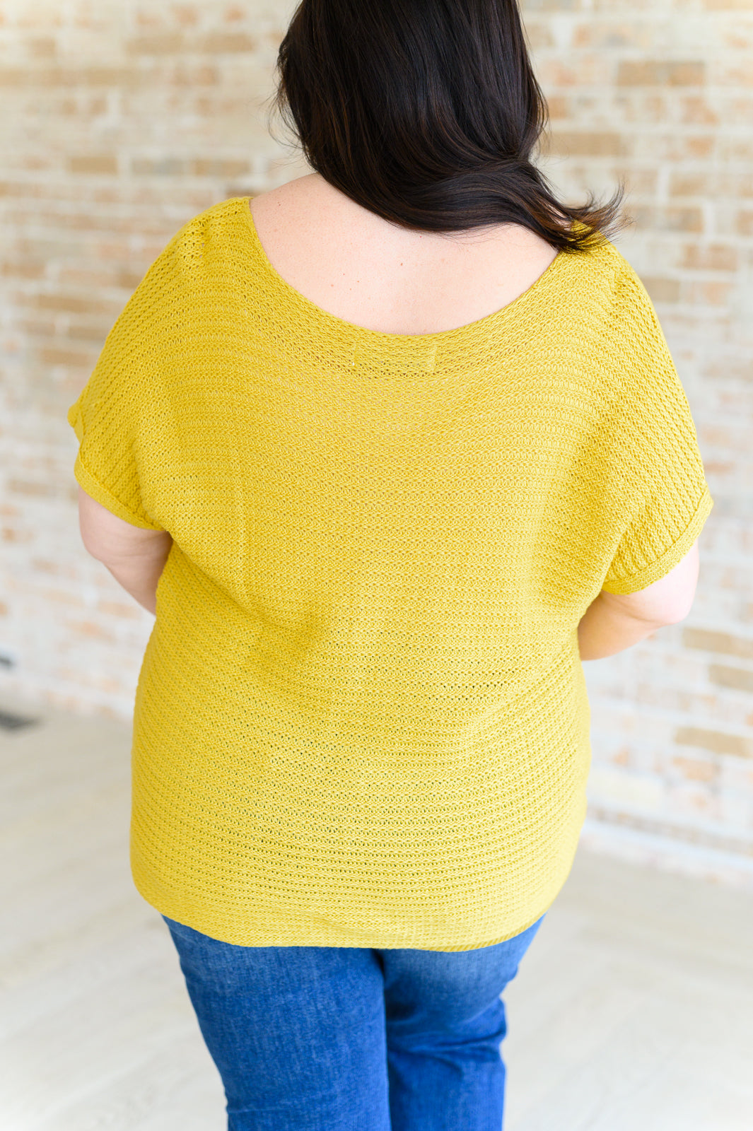 Woman shown from behind wearing vibrant yellow textured knit top with short sleeves and scooped back neckline