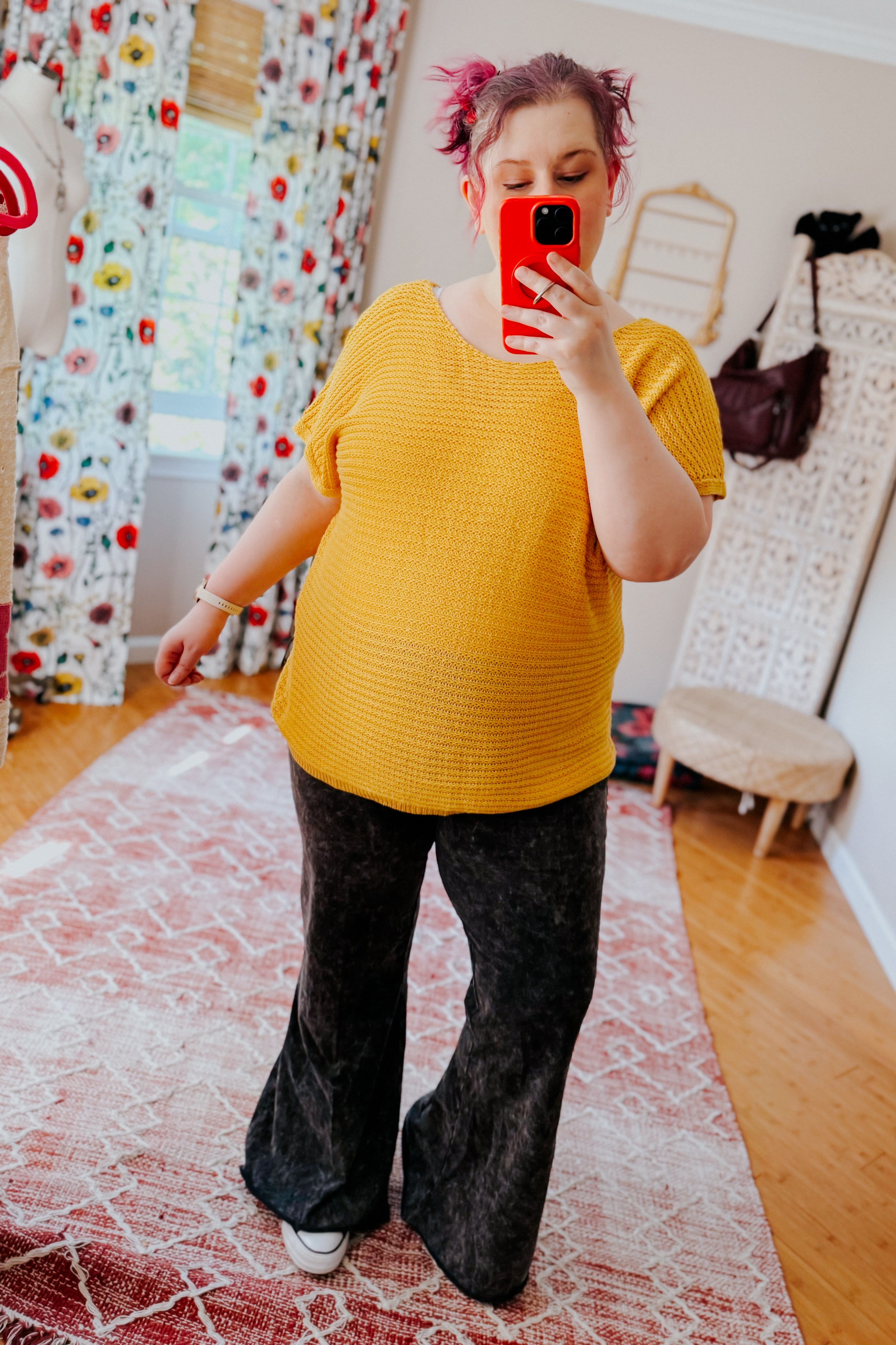 Woman wearing bright yellow textured knit top with short sleeves paired with black wide-leg pants taking mirror selfie indoors