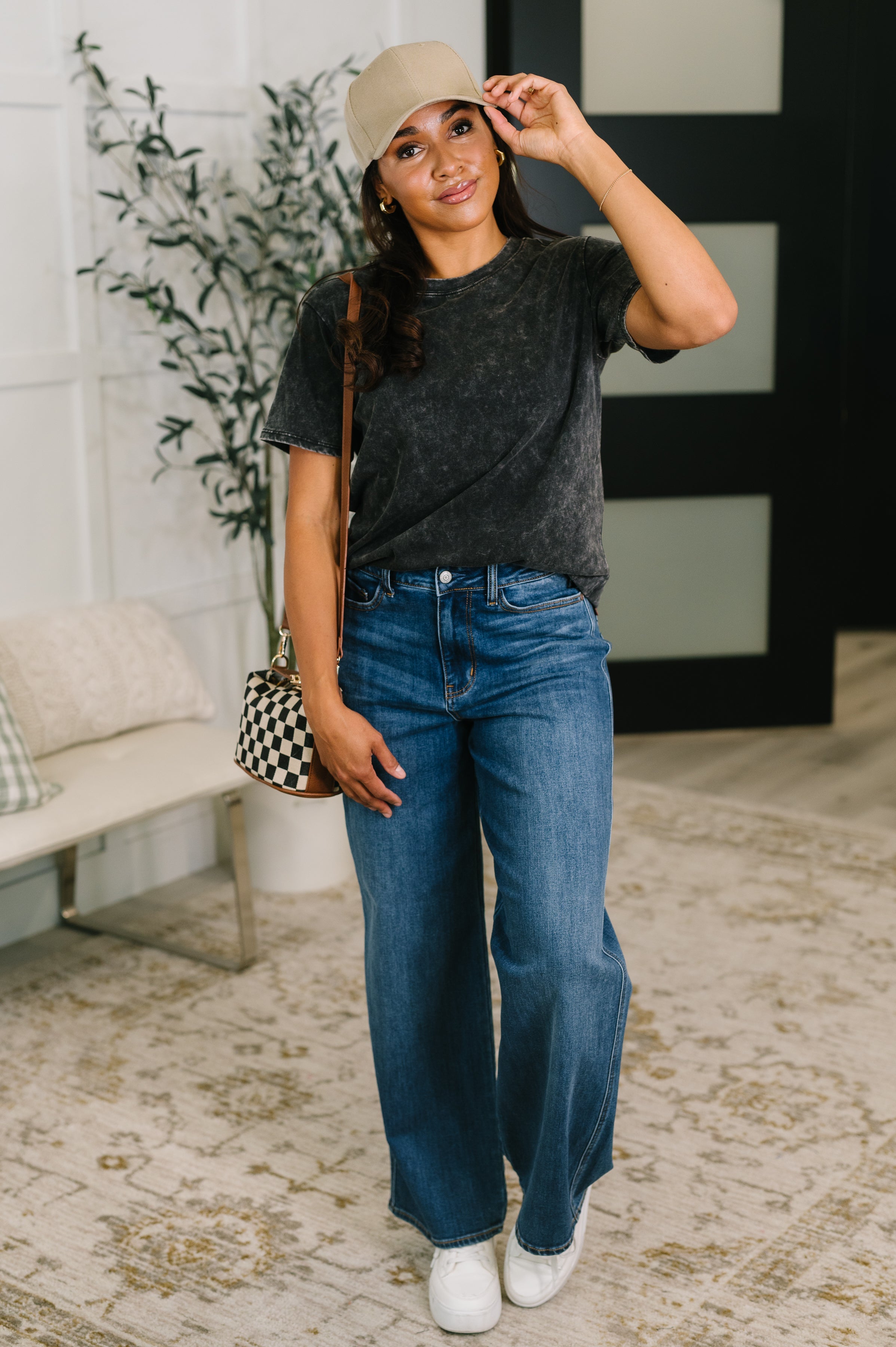 Woman wearing ash black mineral wash tee with high-waisted wide-leg jeans and a beige cap indoors