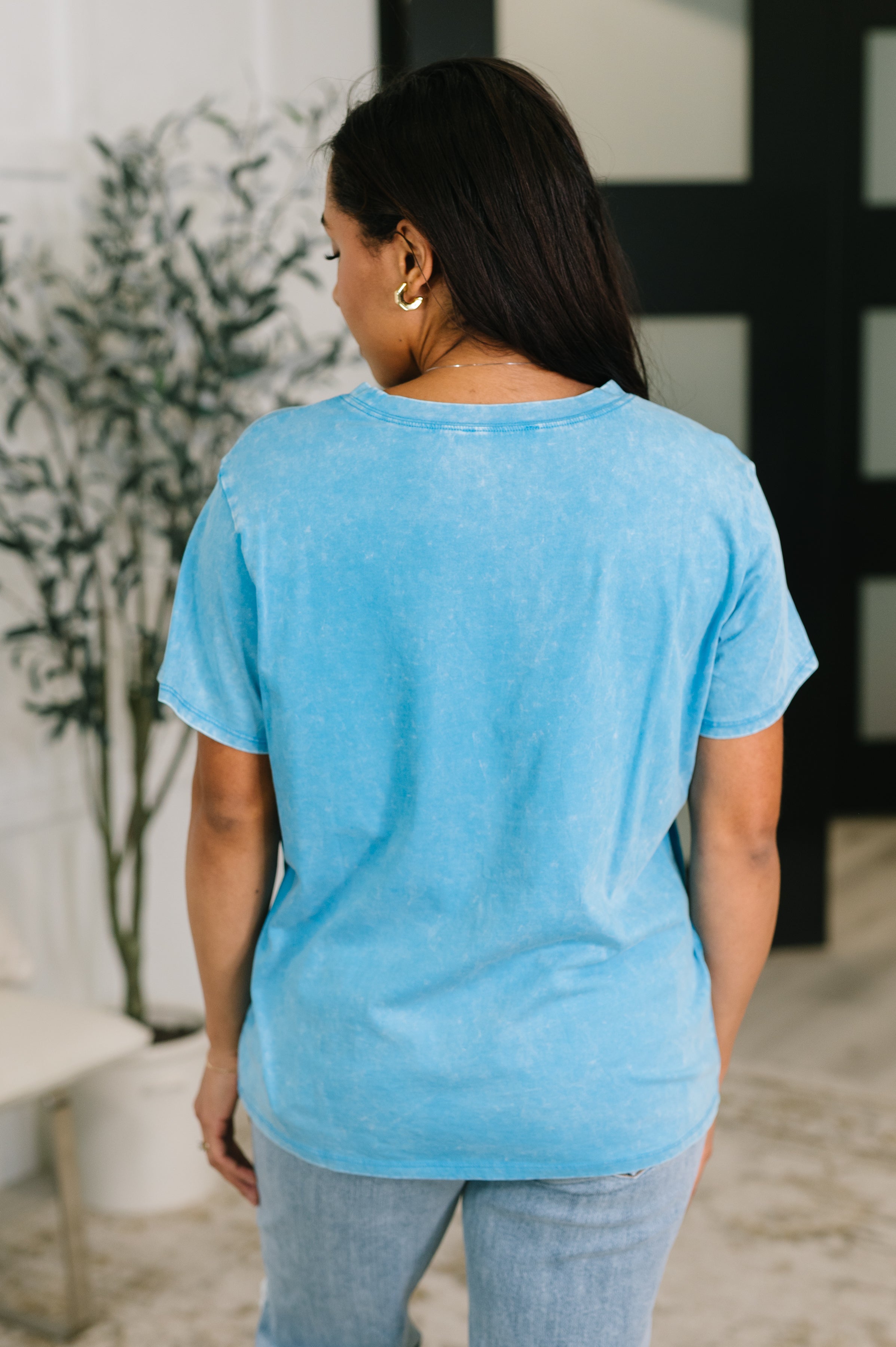 Back view of person wearing a blue mineral wash tee with a relaxed fit paired with light wash jeans indoors