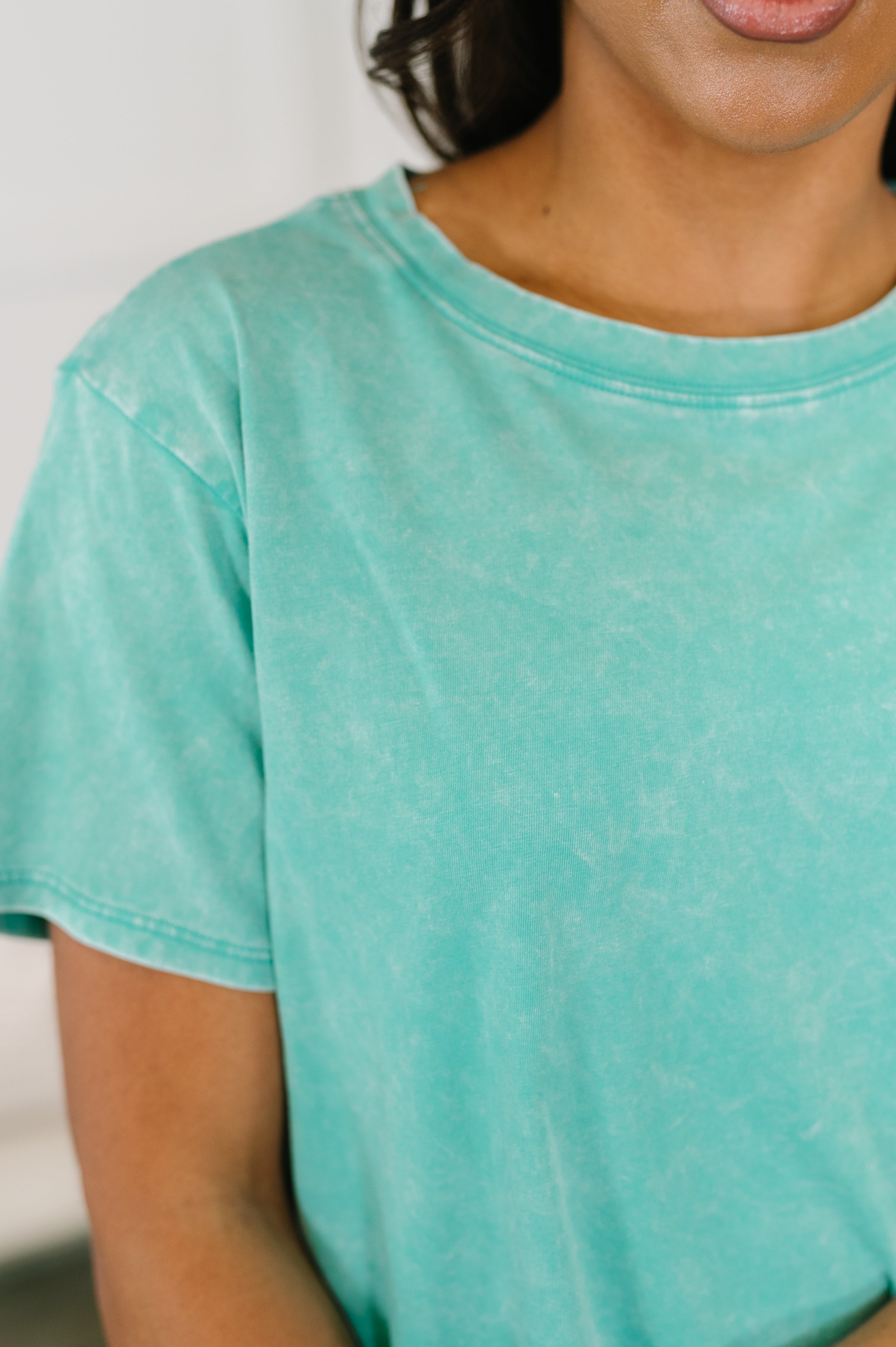 Close-up of plush turquoise mineral wash tee with crew neck and short sleeves on woman with medium skin tone