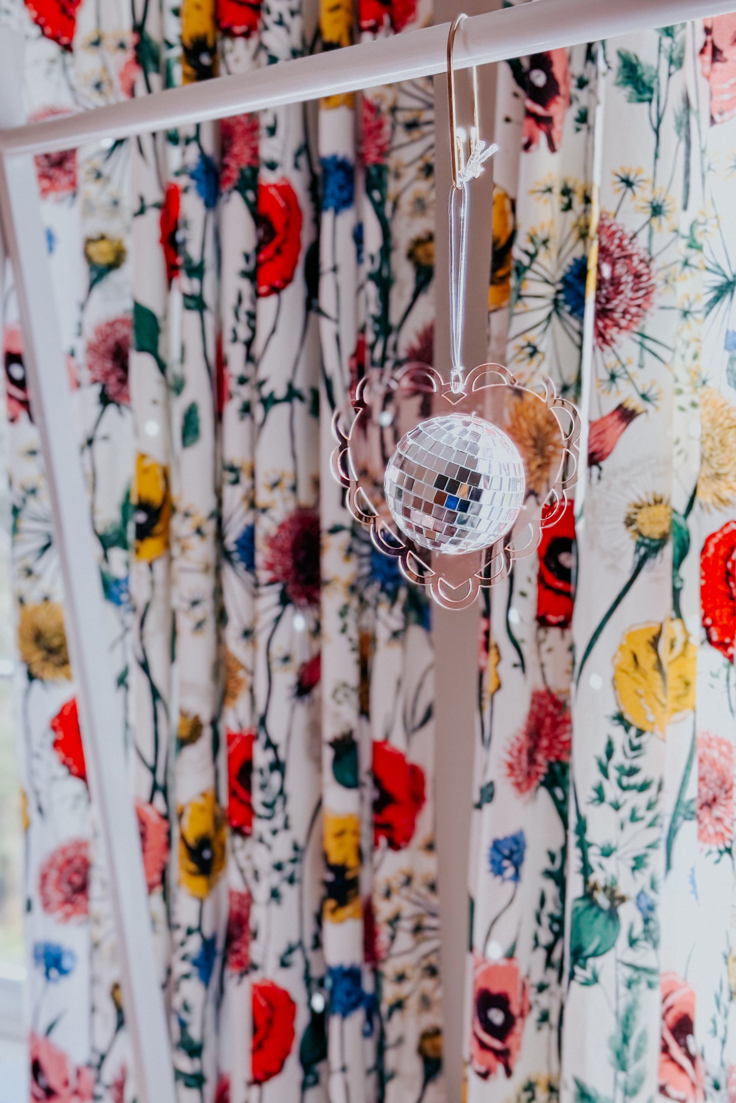 Soft pink scalloped heart sun catcher with hanging mini disco ball in front of vibrant floral curtain background