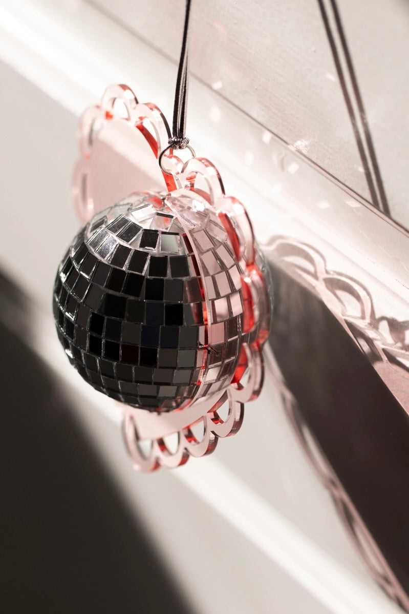 Soft pink scalloped heart frame holding reflective mini disco ball hanging by black cord casting shadow on wall