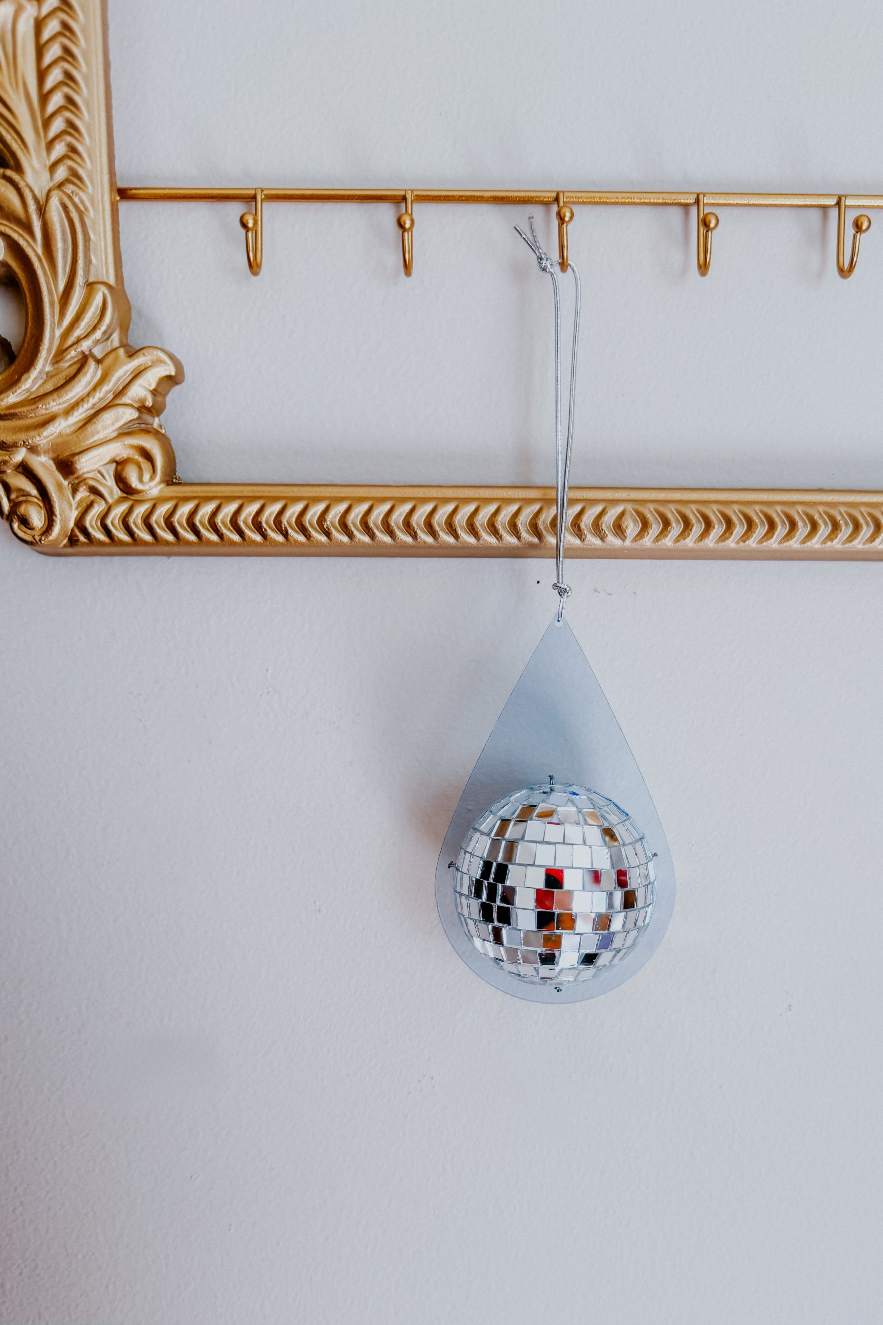 Light blue teardrop shape with a reflective mini disco ball suspended by silver string on gold hook rack