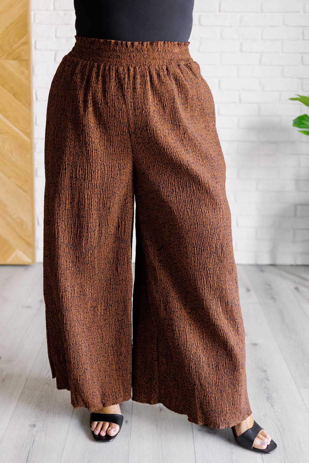 Front view of brown Harmony high rise wide leg pants with elastic waistband and subtle textured design worn with black top and sandals indoors
