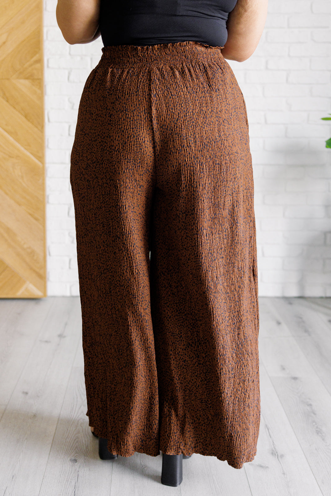 Back view of brown Harmony high rise wide leg pants featuring lightweight textured fabric on model standing indoors