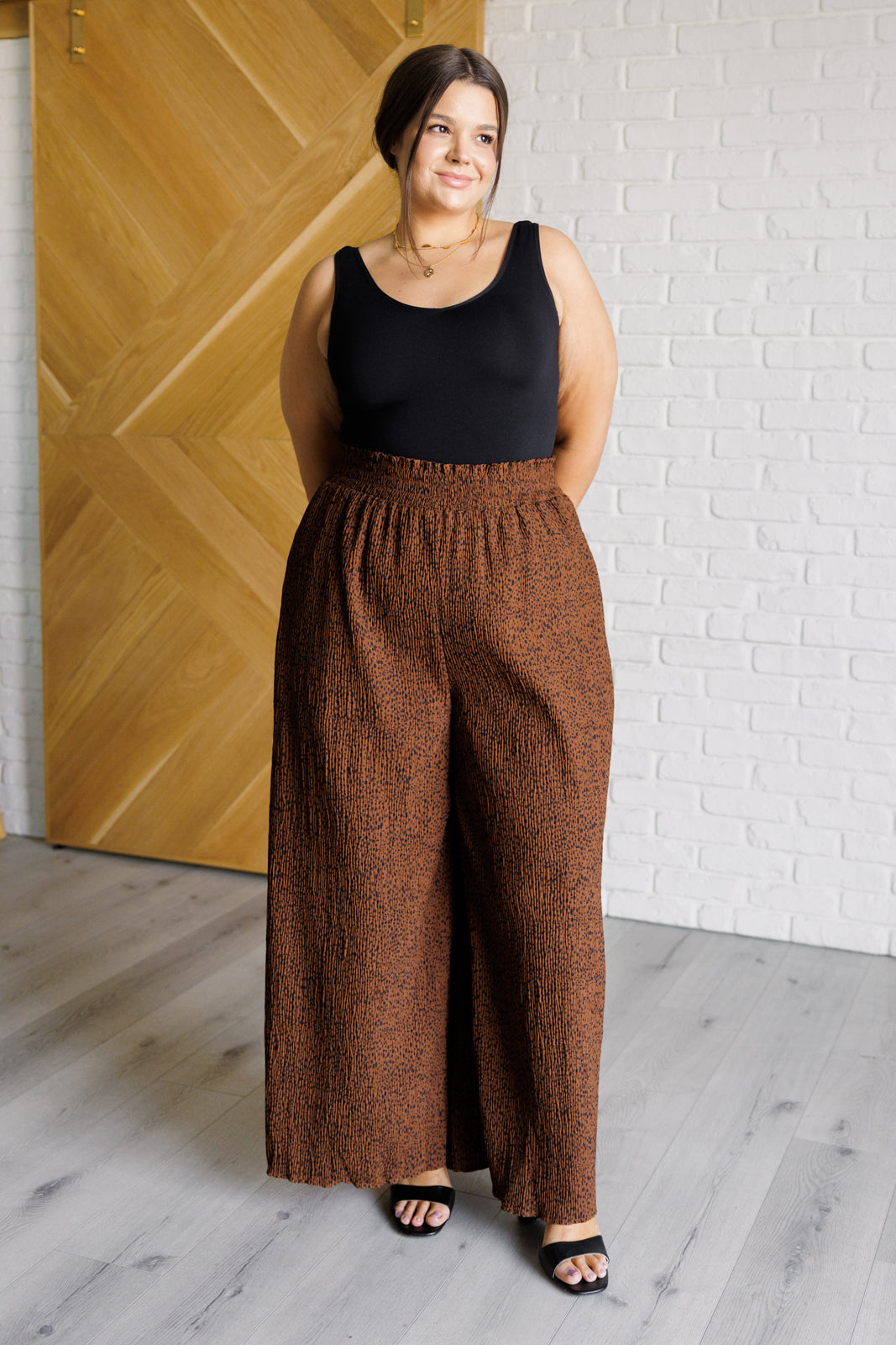 Woman wearing brown textured Harmony high rise wide leg pants with smocked waistband and black sleeveless top indoors