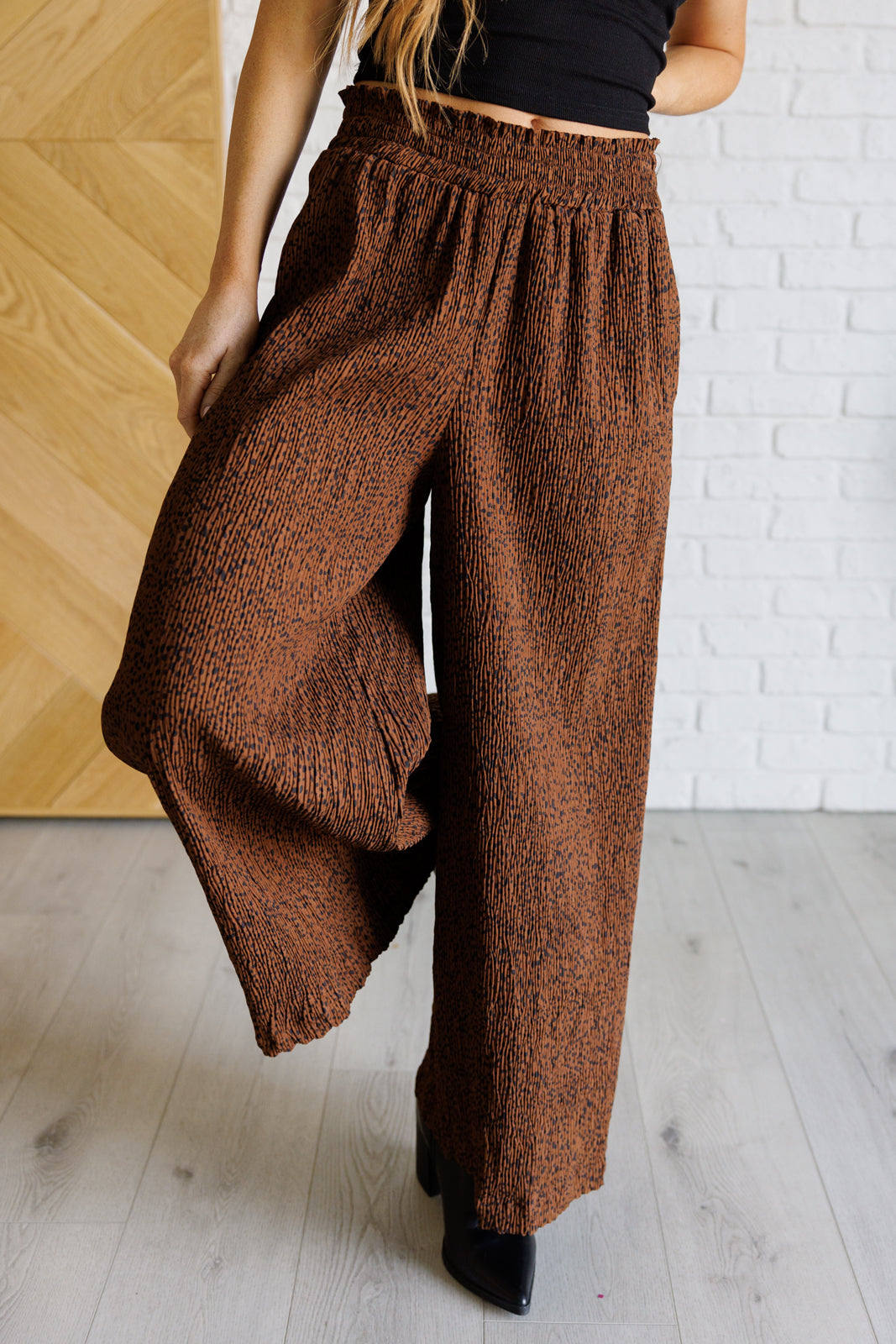 Close-up of brown Harmony high rise wide leg pants with smocked waistband and textured fabric on model indoors