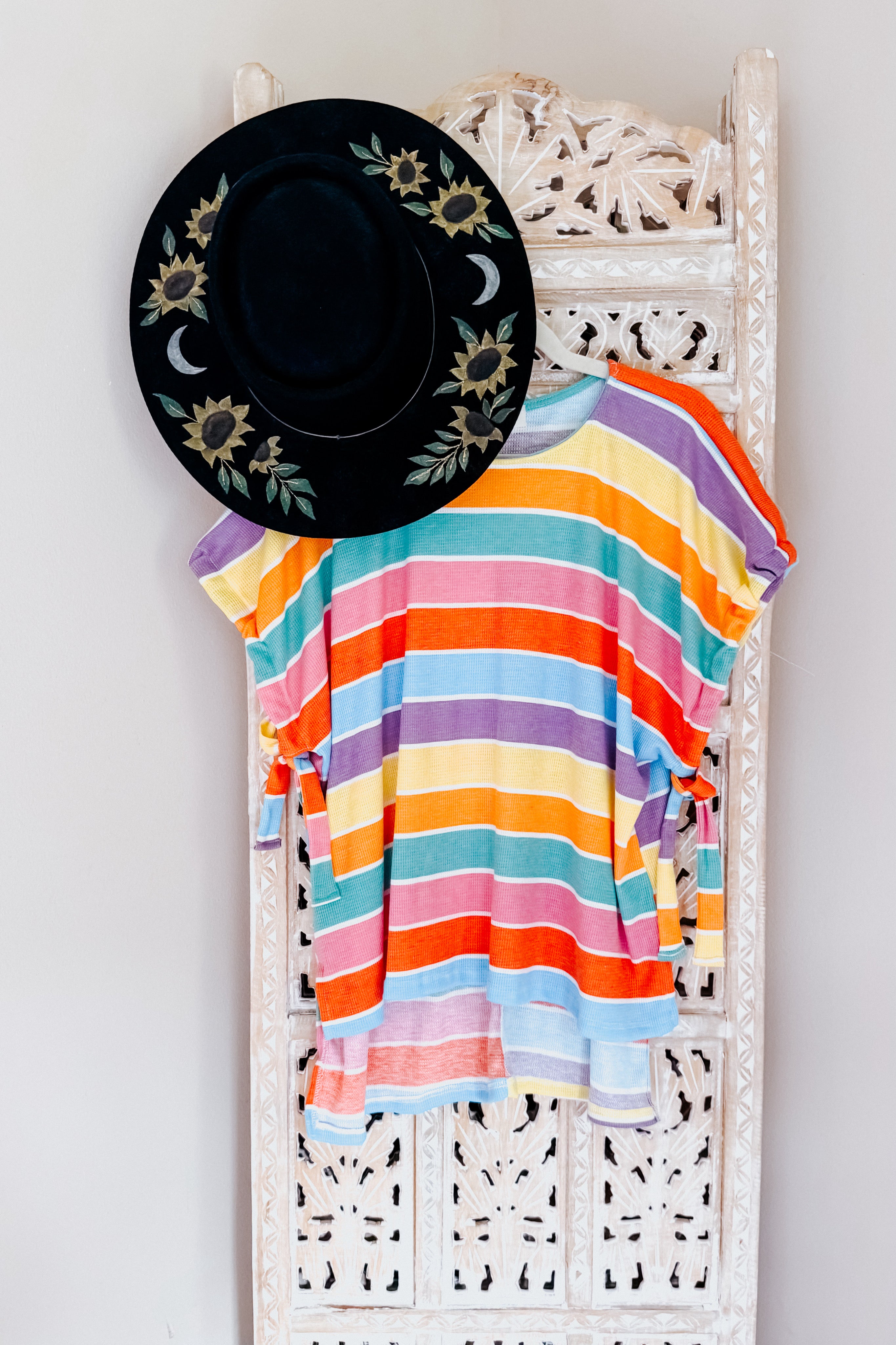 Have Your Heart multicolor striped dolman sleeve top with side ties hanging on carved white wooden panel with black floral sun hat