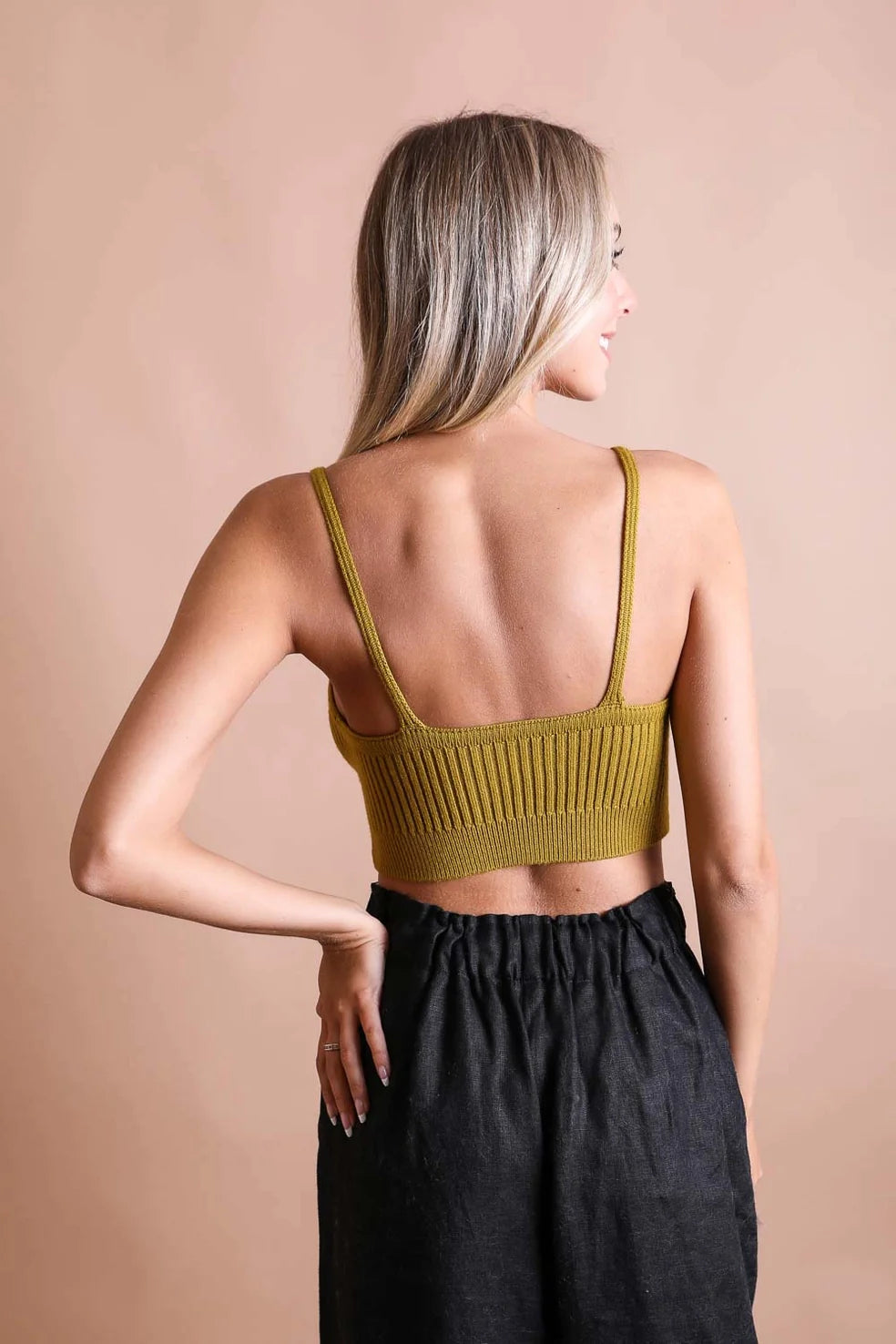 Woman seen from behind wearing mustard hazy baby rib knit brami bralette with thin straps and high-waisted black pants