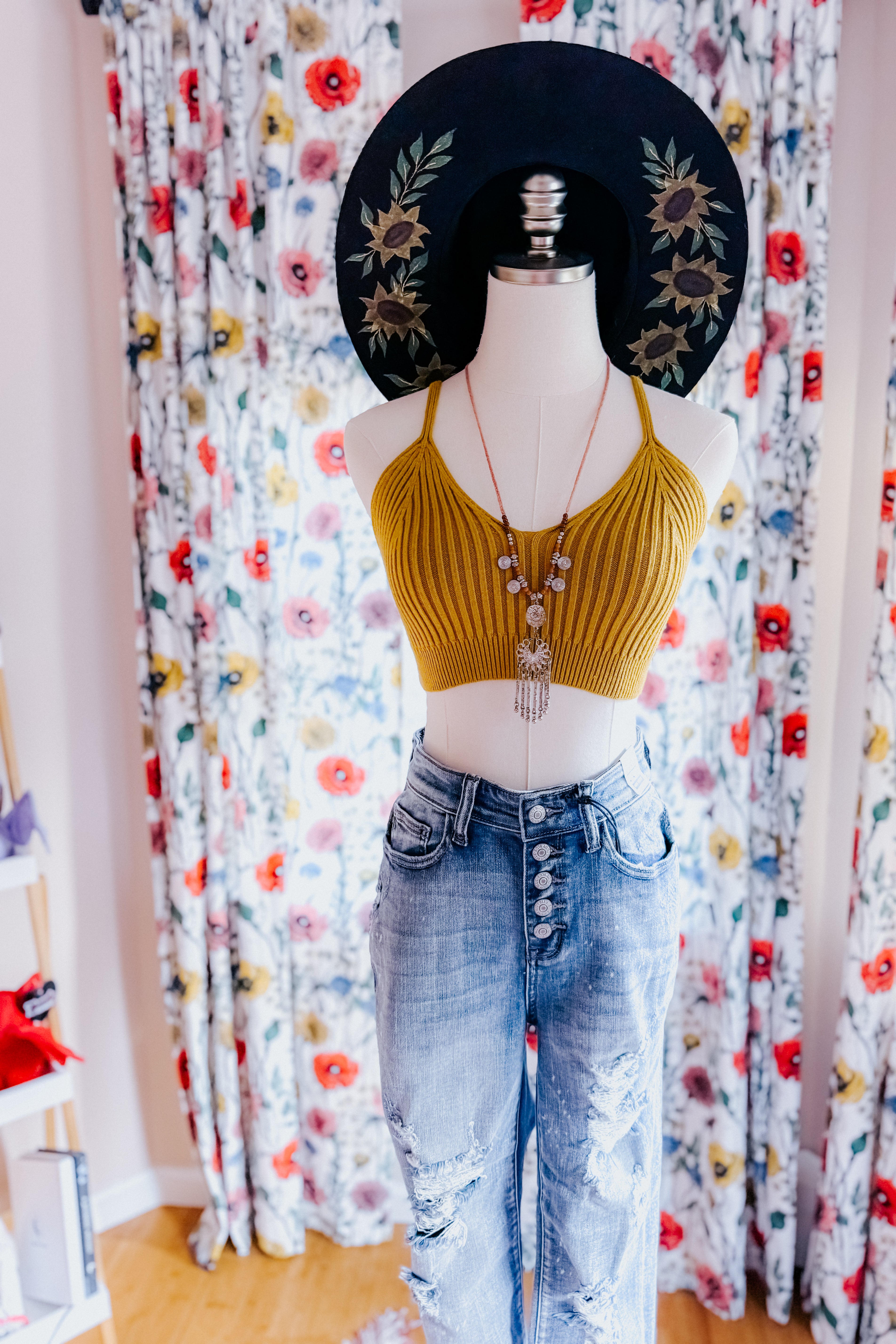 Mannequin dressed in mustard rib knit brami bralette with high-waisted distressed denim jeans and black wide-brim hat indoors