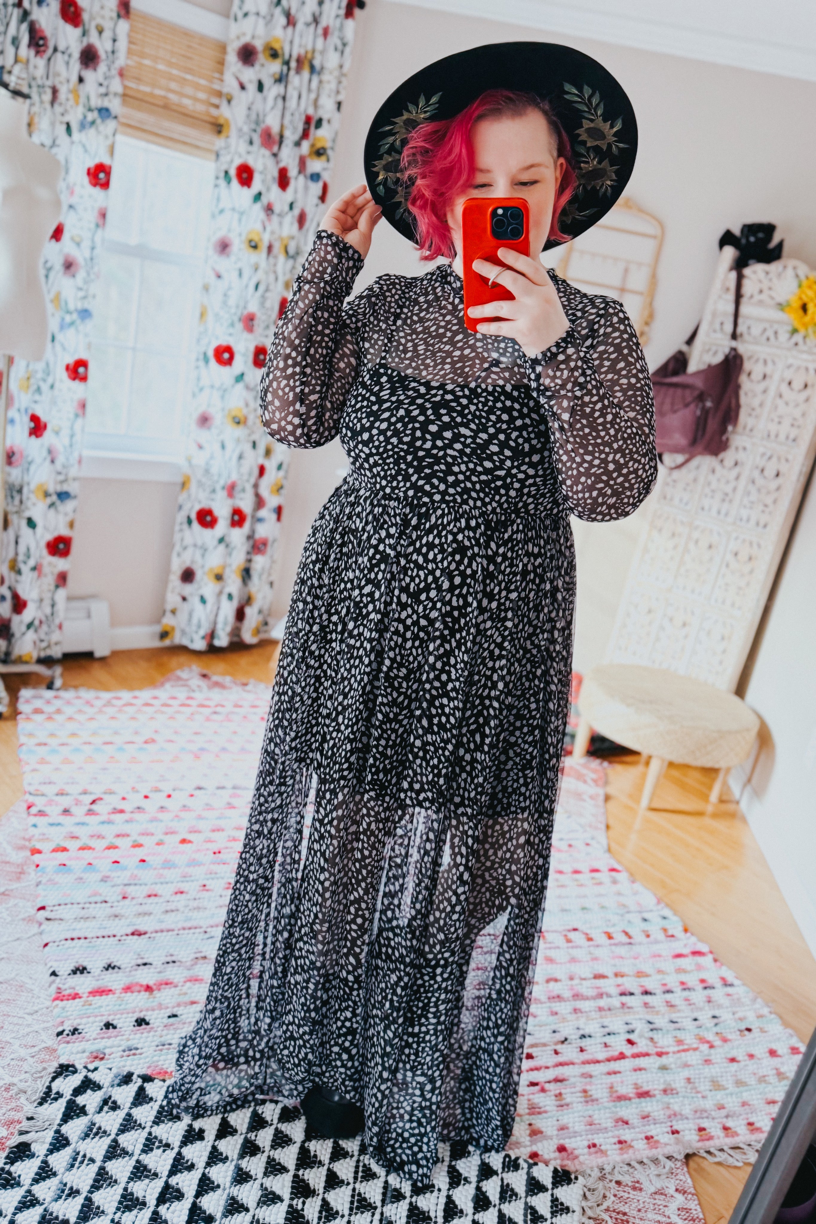 Woman in black Hendrix long sleeve animal print mesh maxi dress and black floral wide-brim hat taking selfie indoors