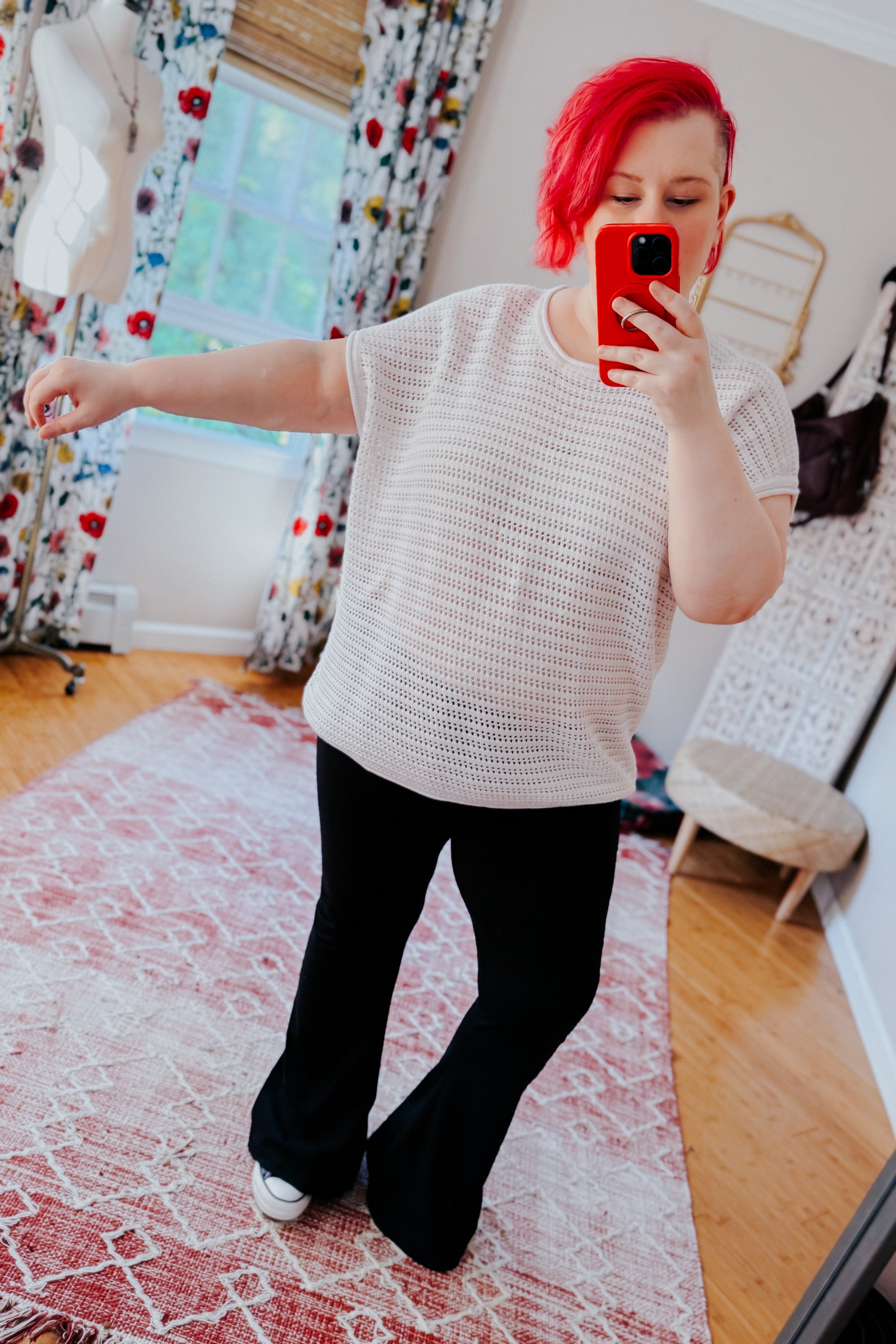 Woman wearing white open knit cap sleeve sweater paired with black flared pants and white sneakers in bright room