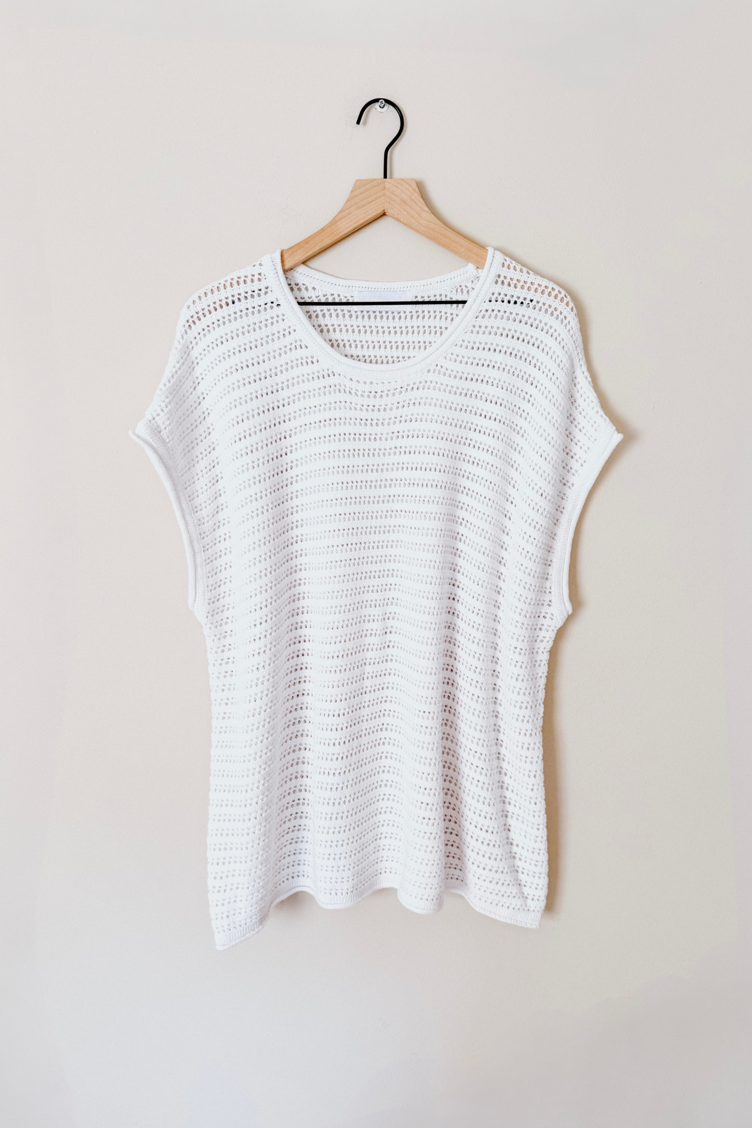 White open knit short sleeve sweater with loose fit hanging on wooden hanger against neutral background