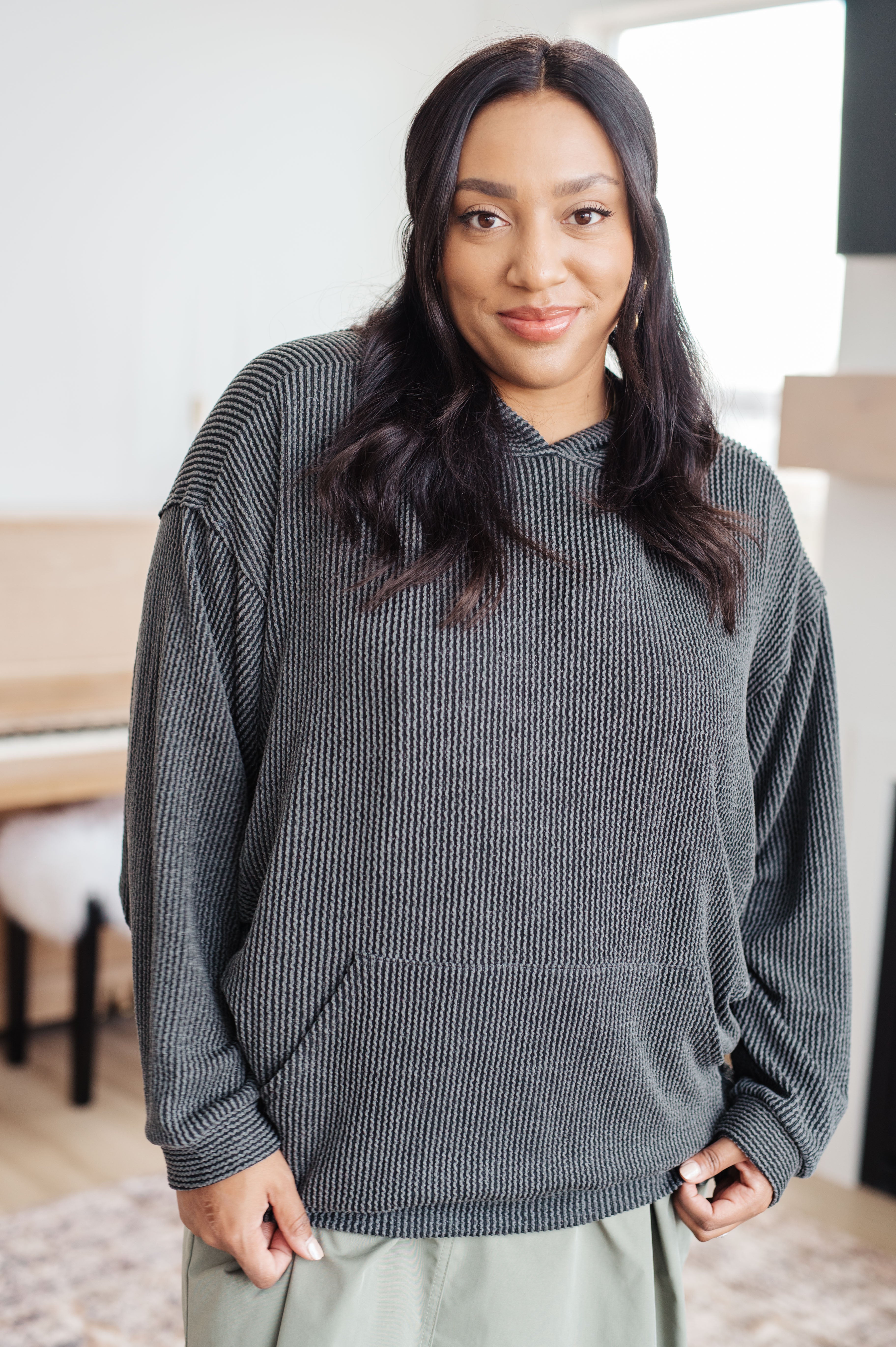 Woman wearing a grey rib knit hoodie over green skirt against an indoor setting.