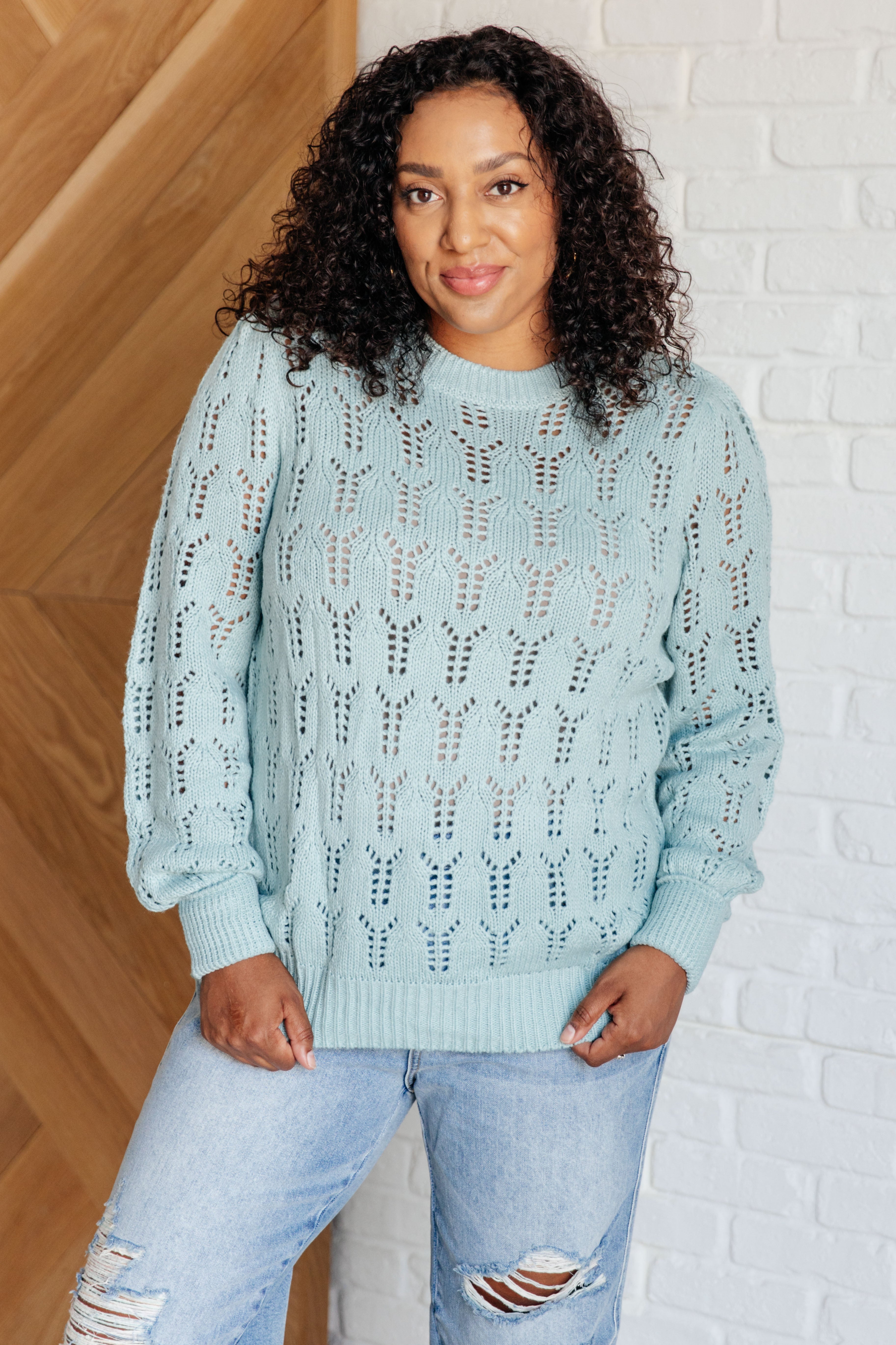 Woman wearing a light blue sheer knit sweater with a unique openwork pattern and relaxed fit paired with ripped jeans
