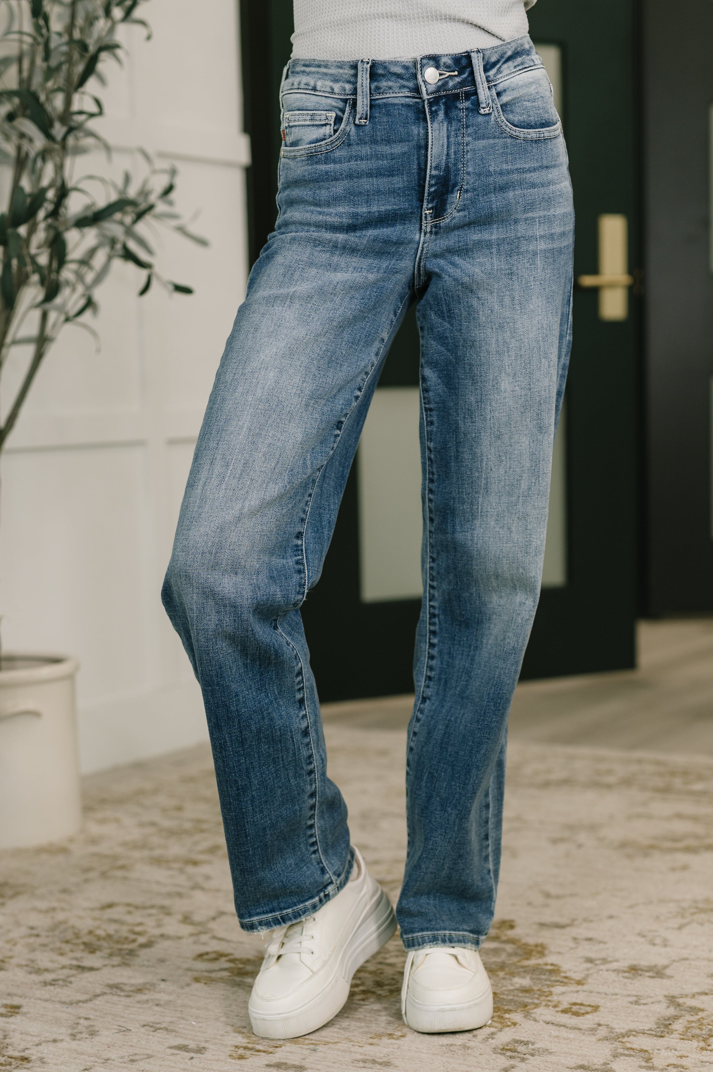 Close-up of mid-rise straight blue jeans styled with white sneakers in casual indoor setting