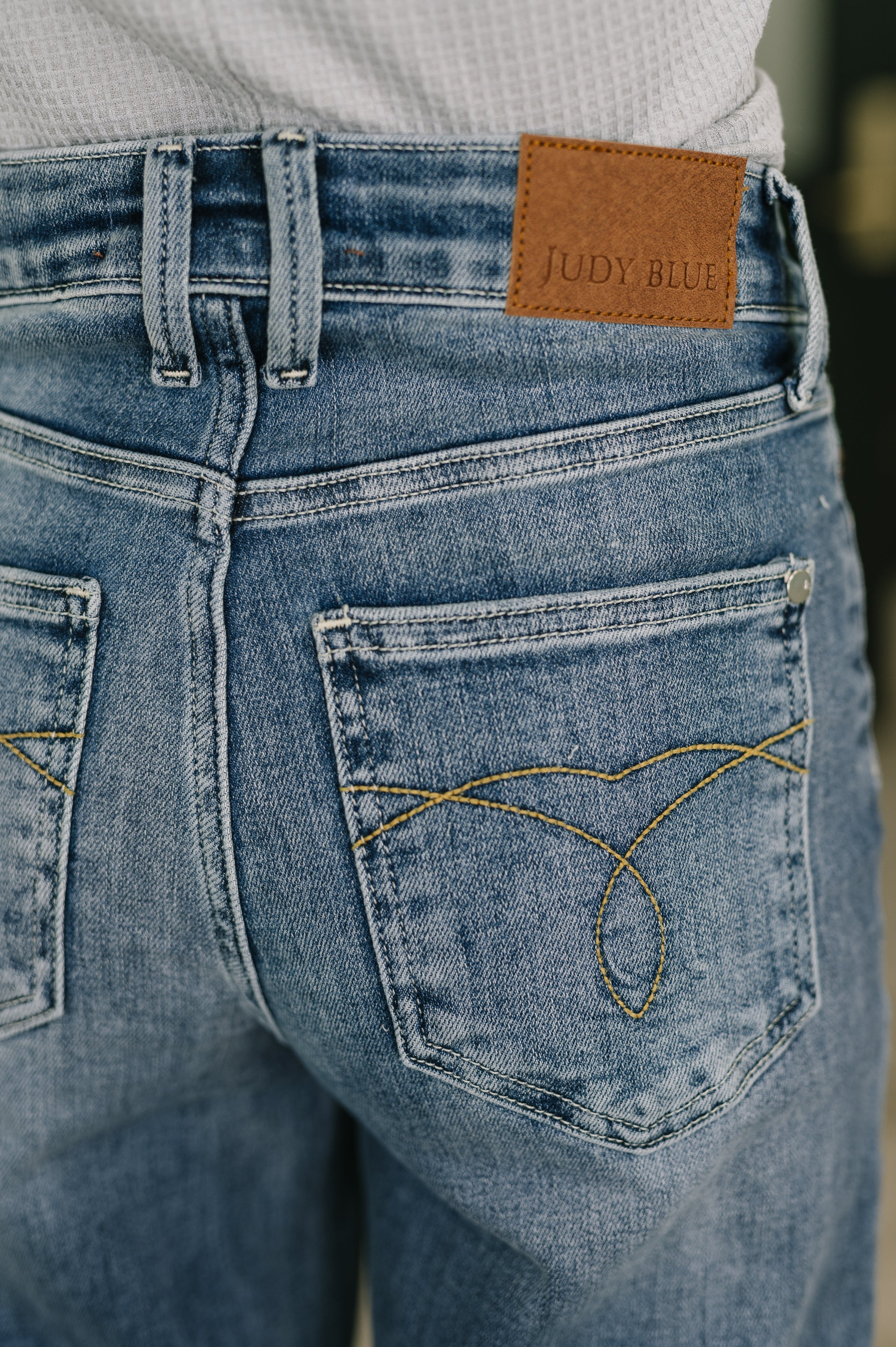 Close-up of blue mid-rise straight jeans with decorative stitching on back pockets and leather brand patch