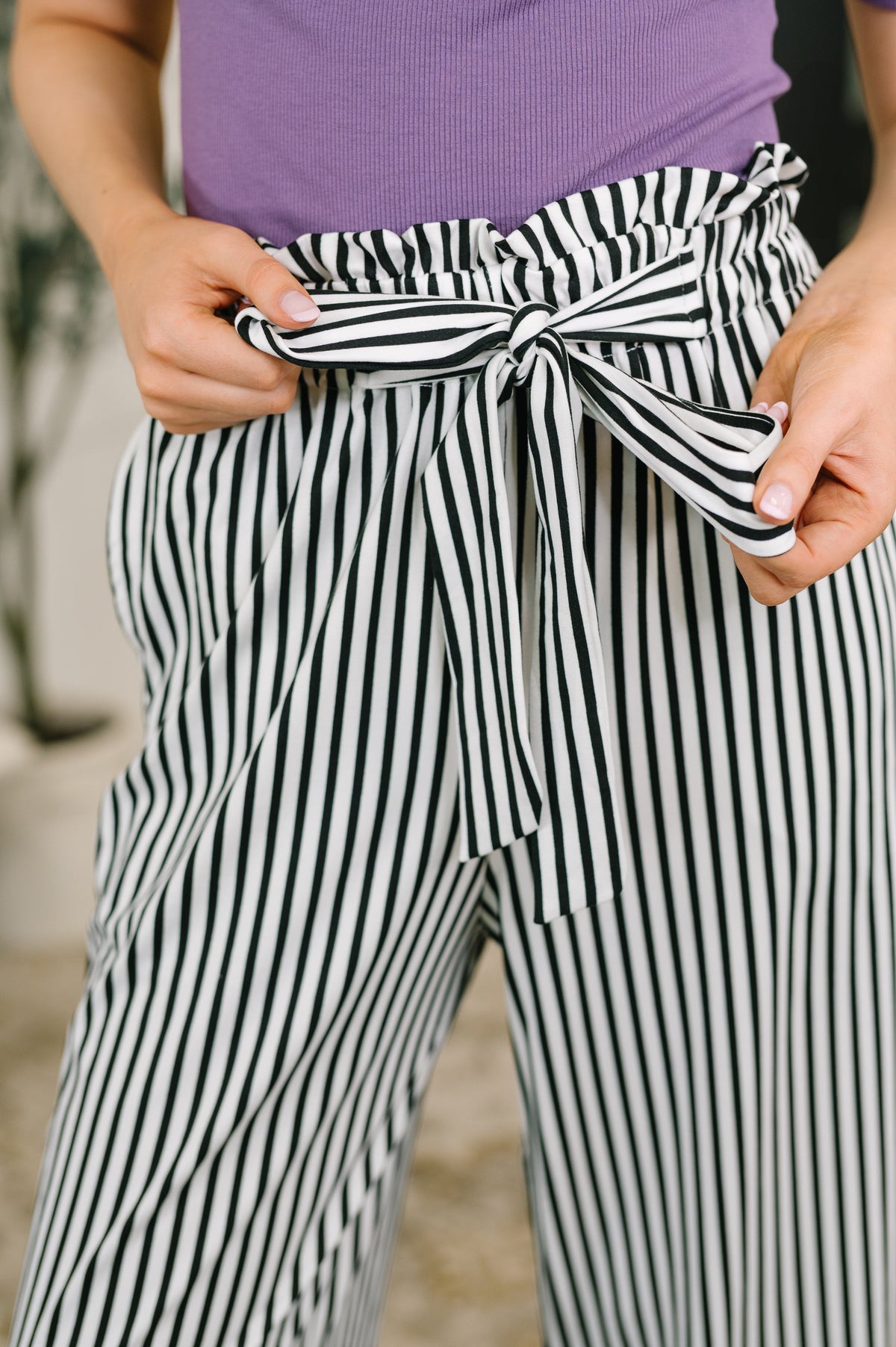 Person wearing black and white striped high waisted wide leg trousers with a tied paperbag waist and purple top