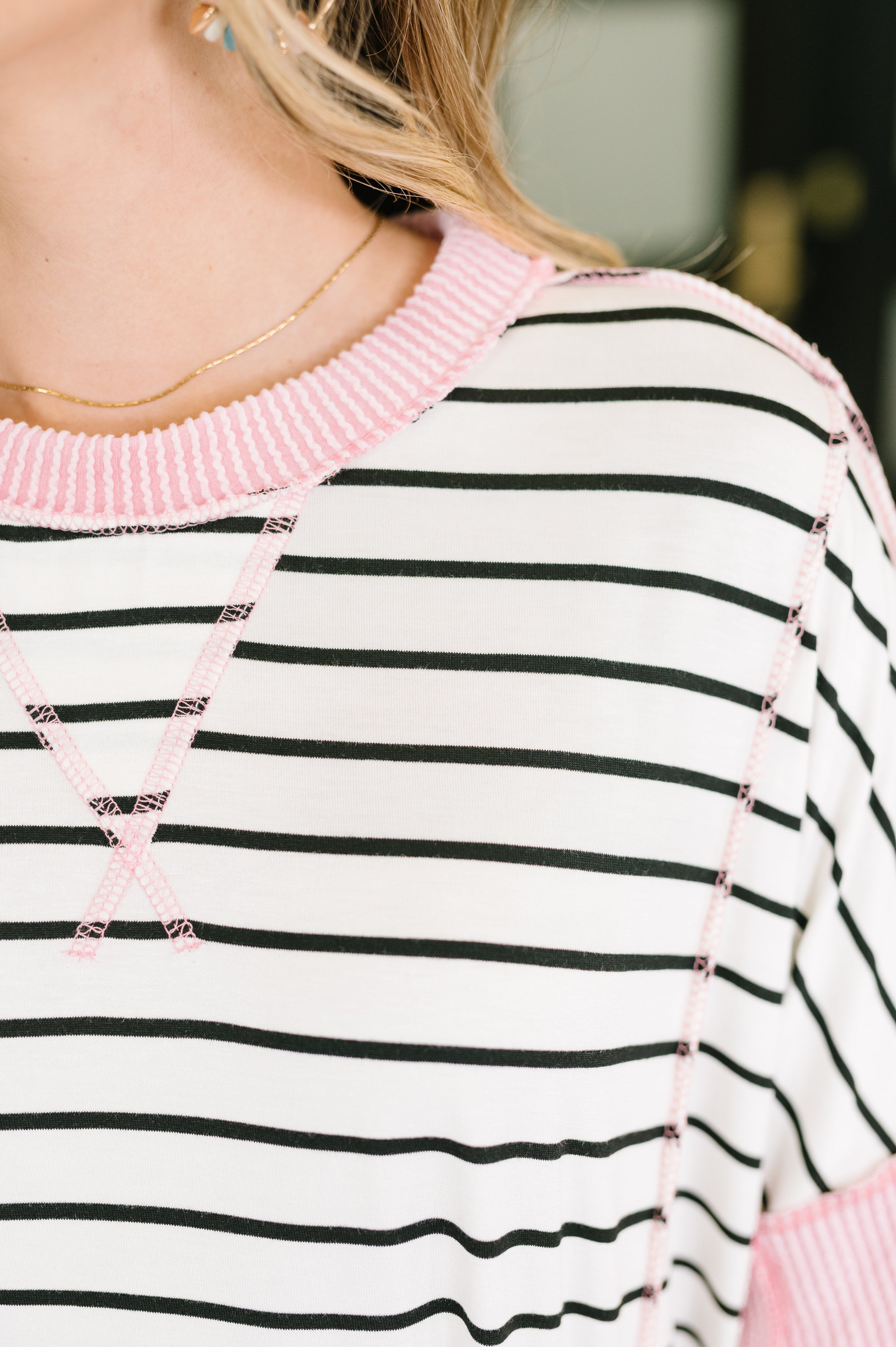 Close-up of ivory and black striped top with pink ribbed neckline and contrast stitch detailing on shoulder and chest