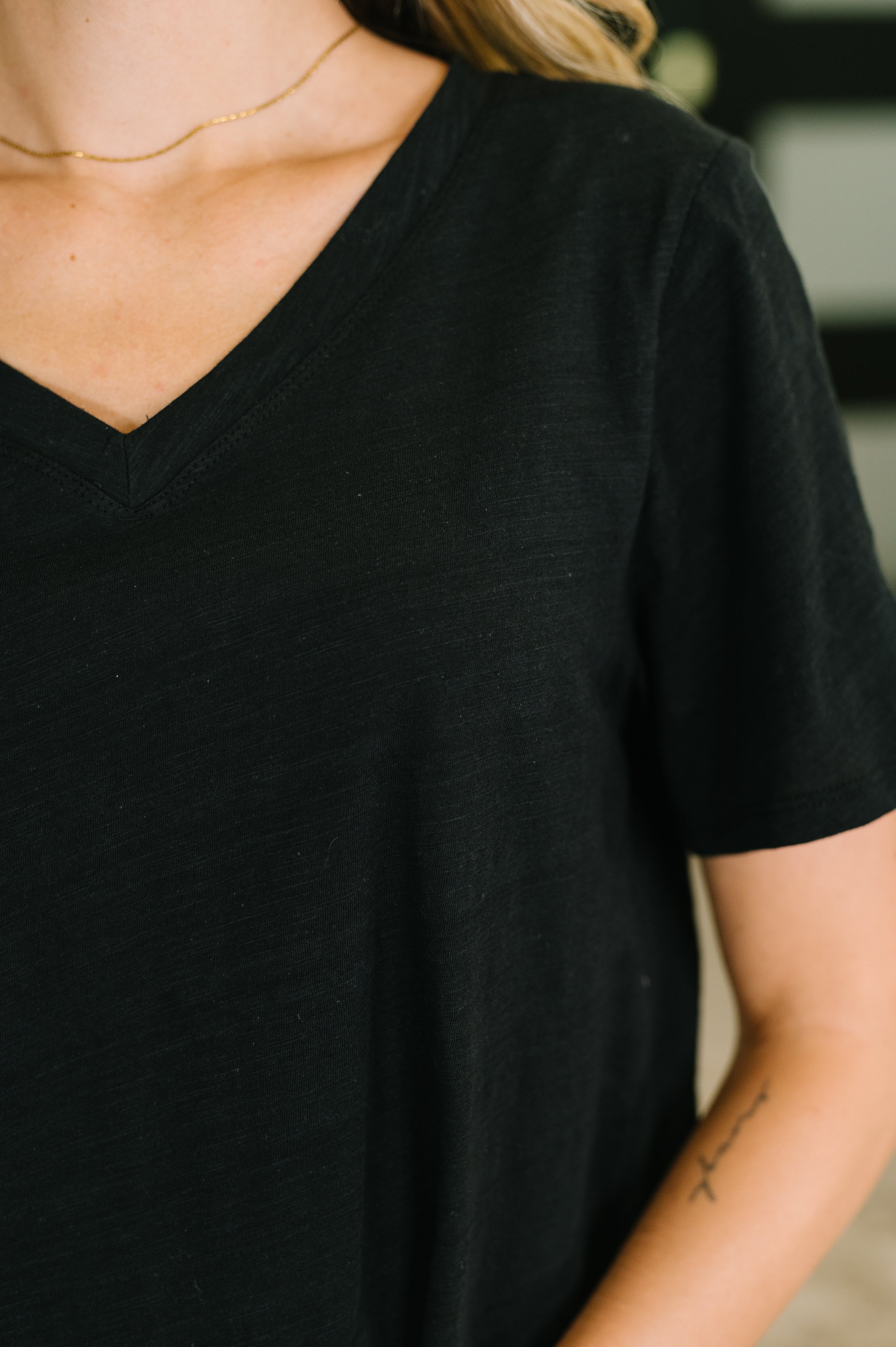 Close-up of relaxed fit black V-neck tee on woman wearing delicate gold chain necklace indoors