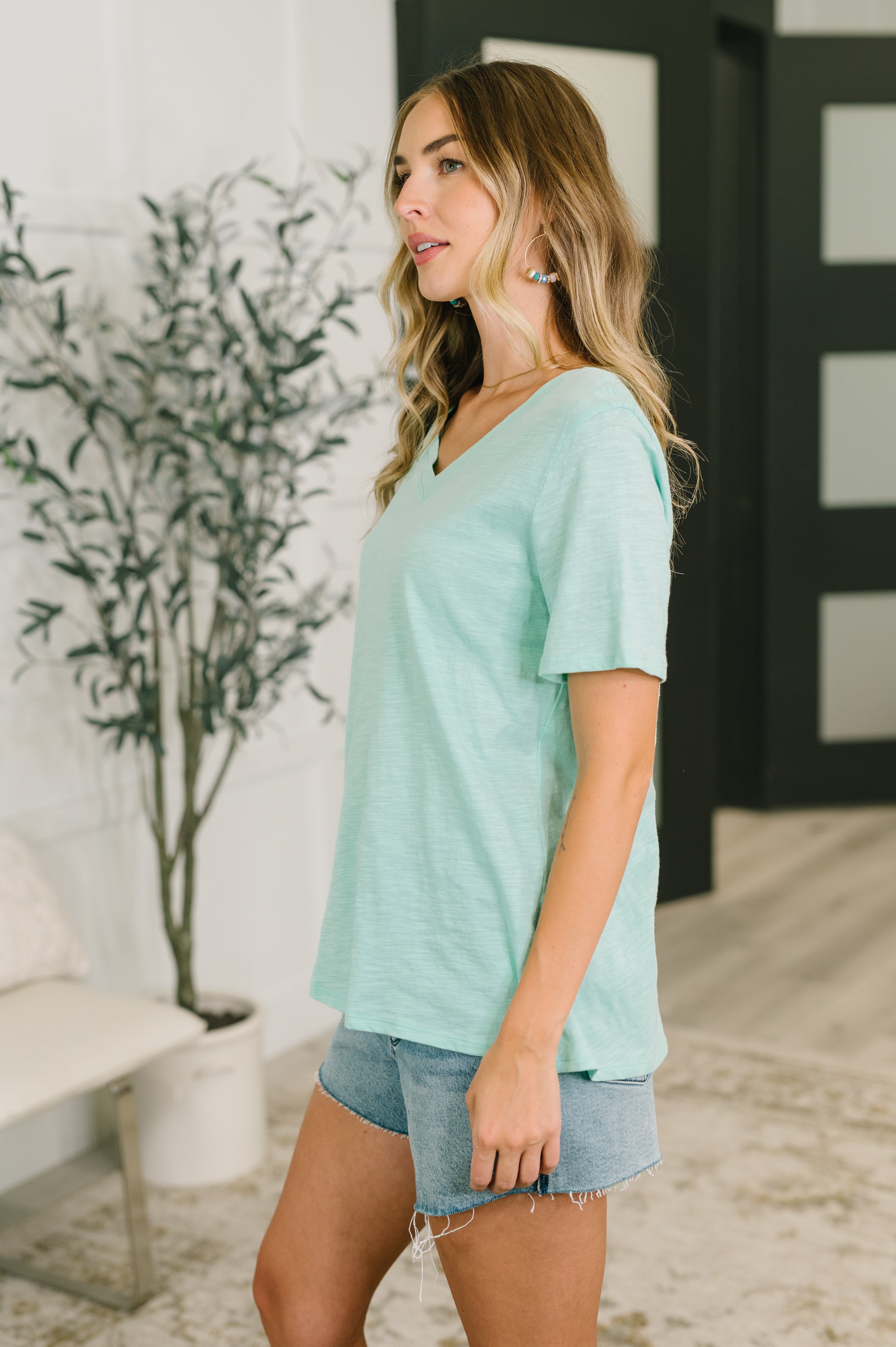 Woman wearing relaxed fit mint V-neck tee with short sleeves and light denim shorts indoors