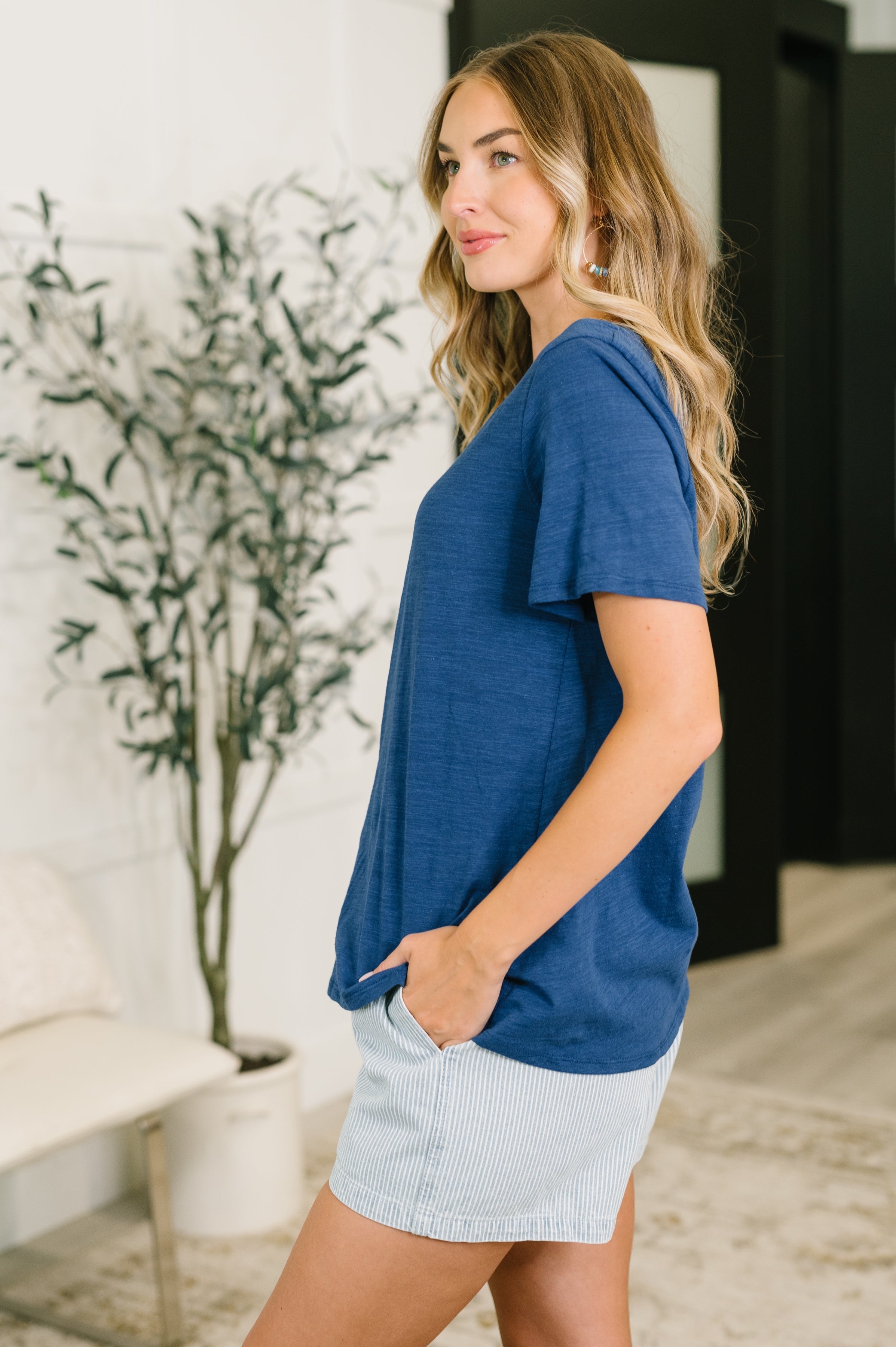Side view of woman wearing navy relaxed v-neck tee with short sleeves and striped shorts indoors