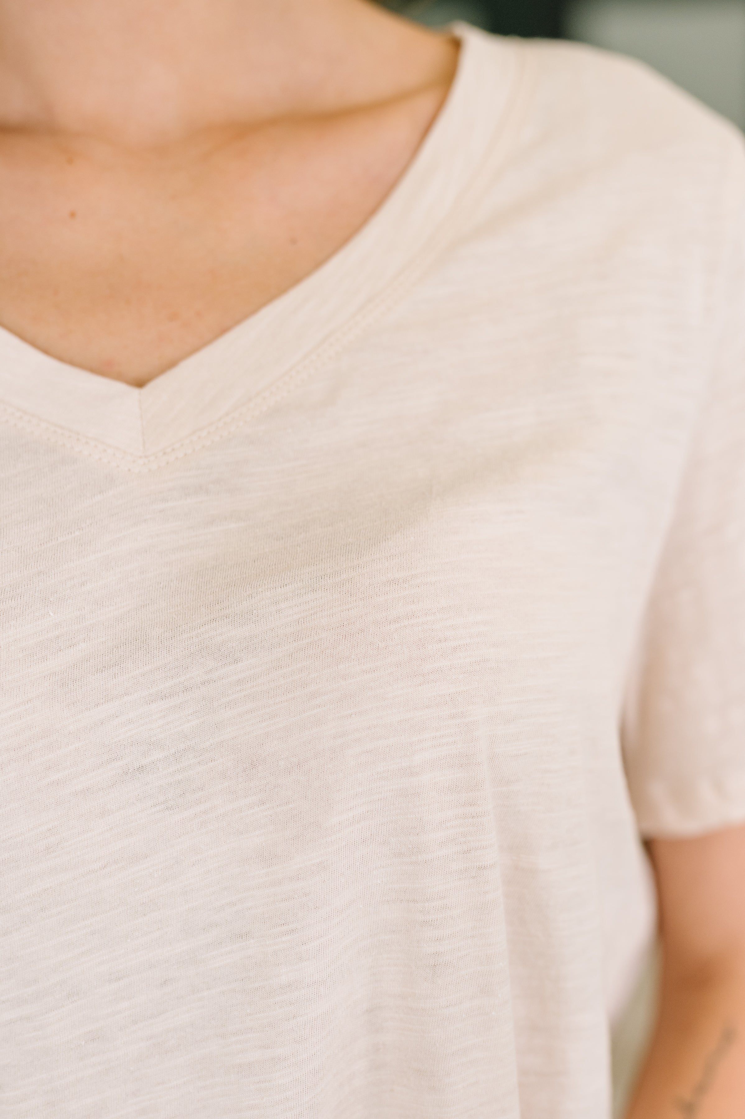 Close-up of soft oatmeal-colored V-neck tee with subtle texture and relaxed fit on a woman’s upper torso