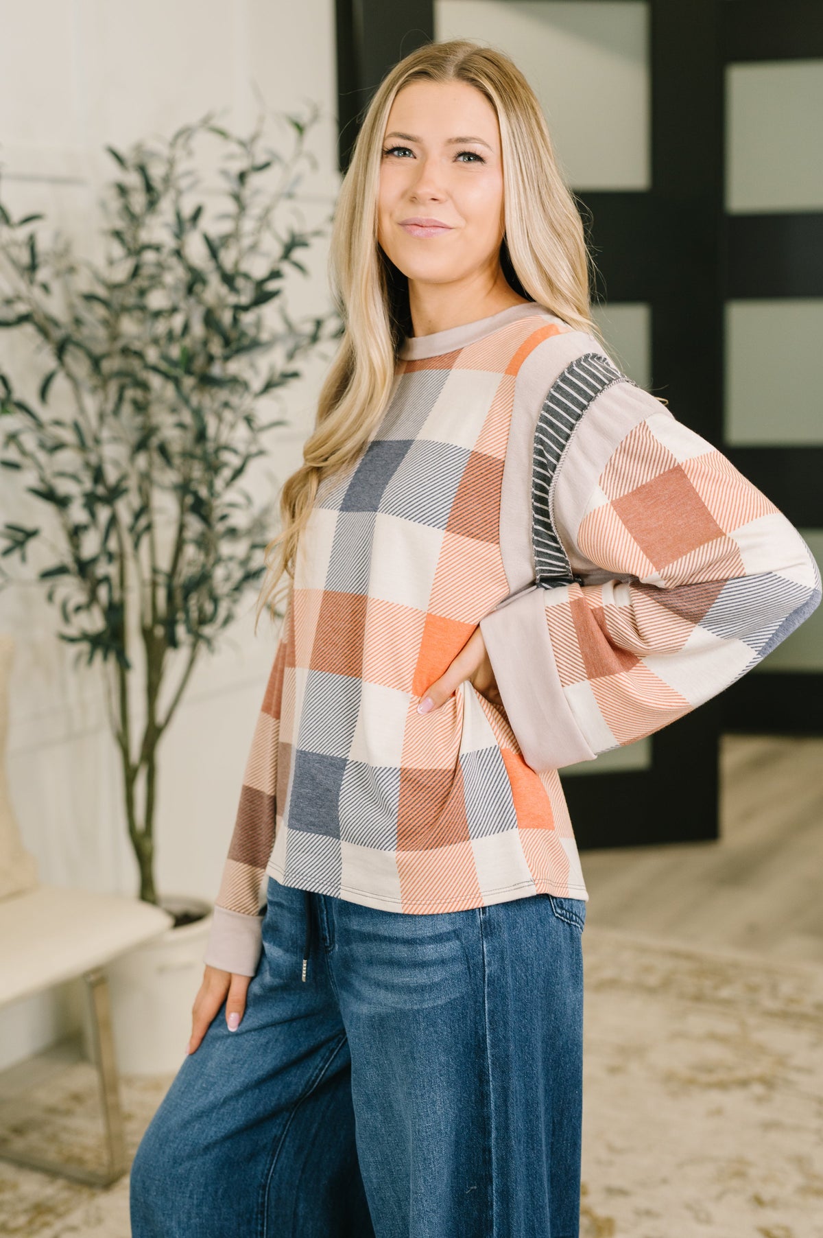 Woman models an orange plaid relaxed top with balloon sleeves and blue jeans in a bright modern interior
