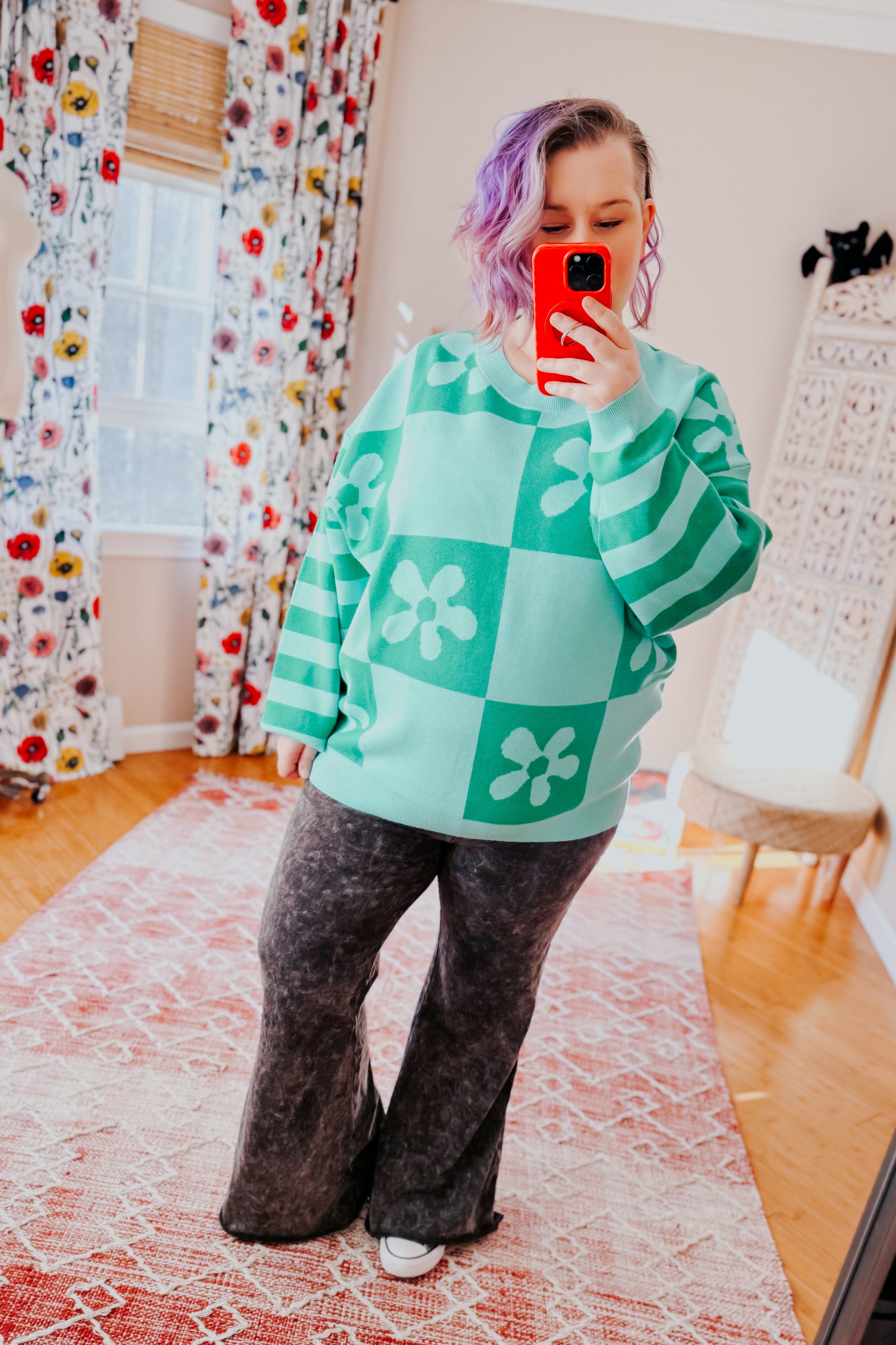 Woman wearing a checkered floral print mint sweater over acid wash flared pants in an indoor setting.