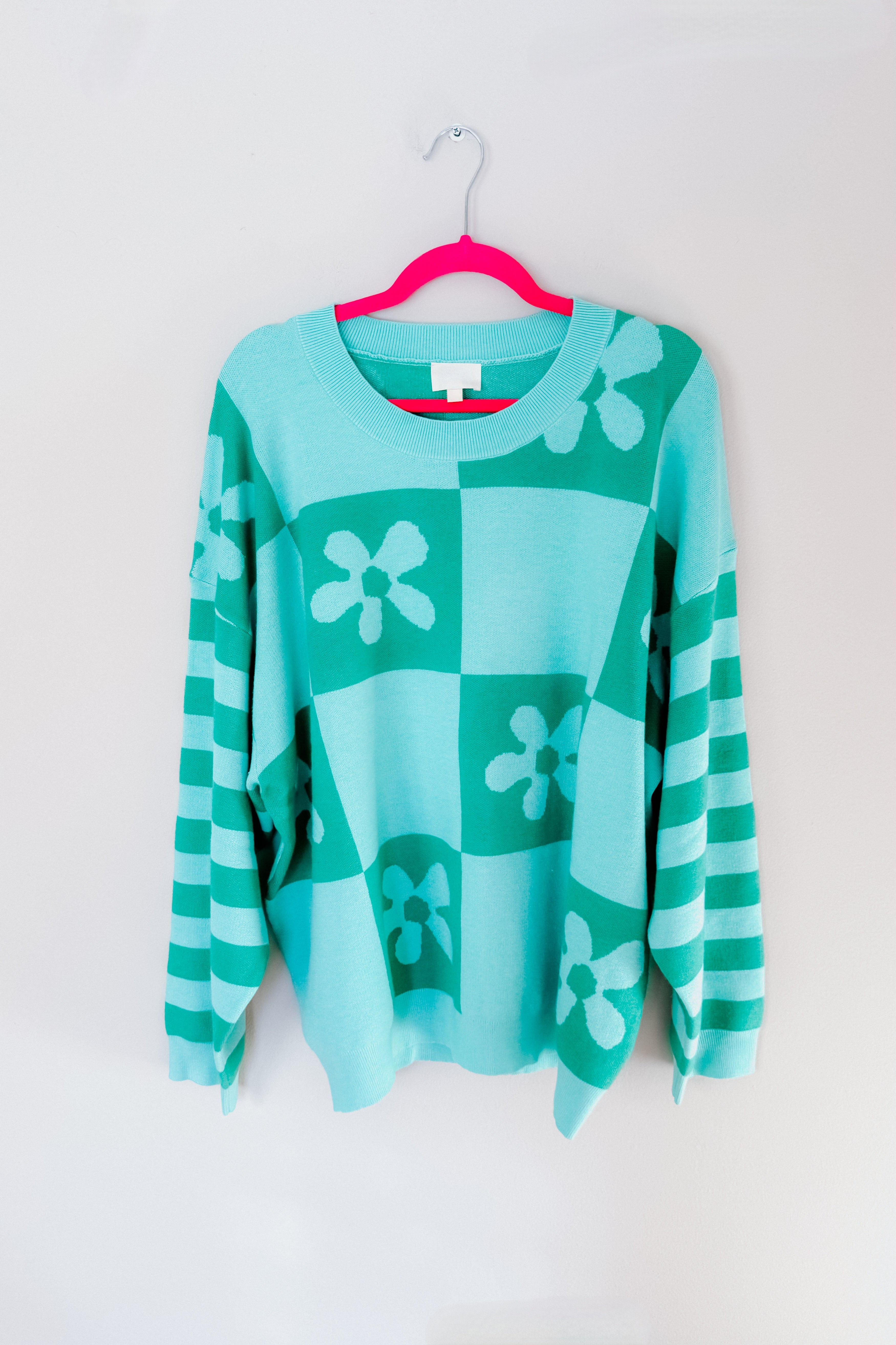 A mint floral checkered print sweater hanging from a pink hanger.