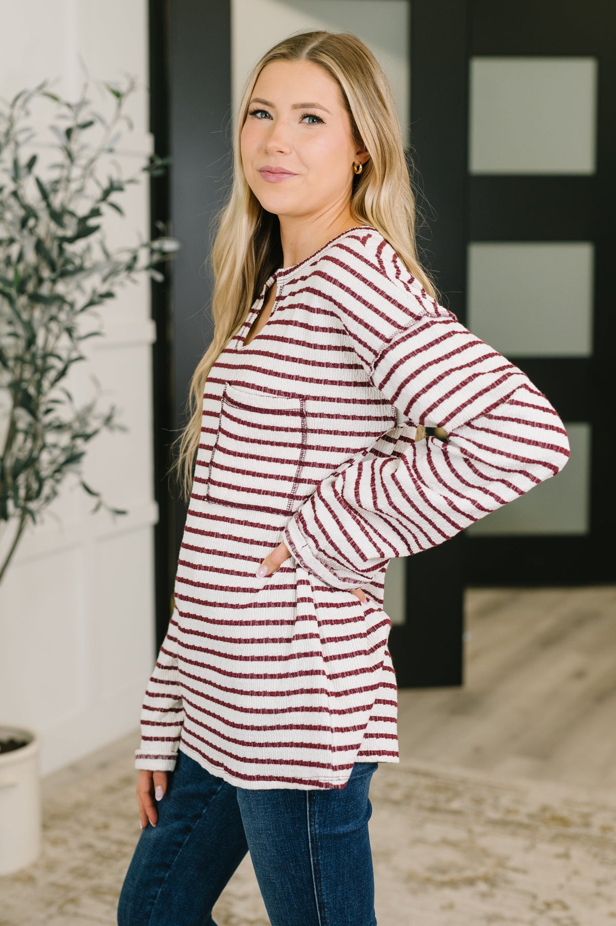Woman wearing a cream and burgundy striped textured knit long sleeve top with relaxed sleeves and dark jeans indoors
