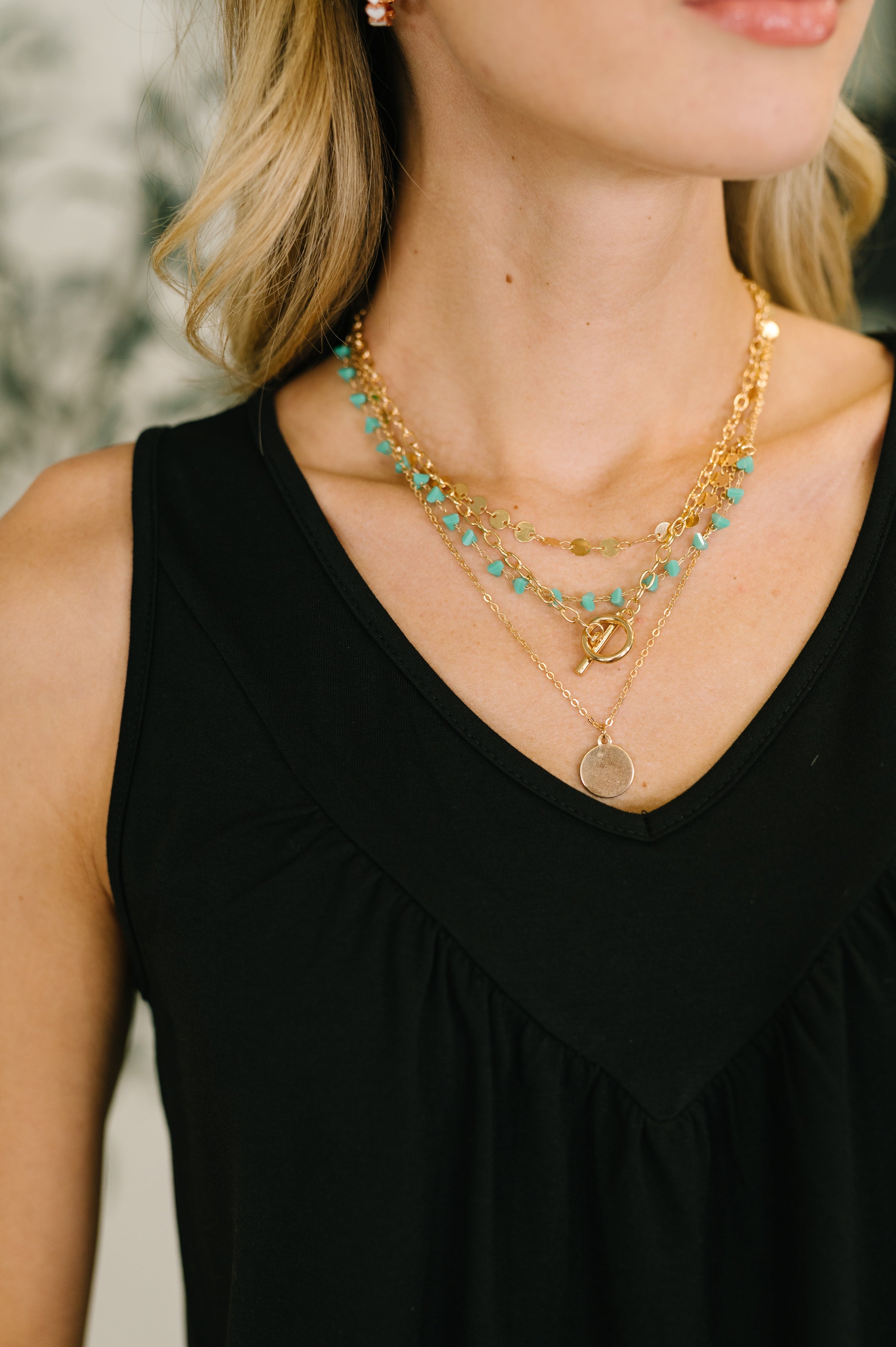 Woman wearing layered gold chain necklaces with turquoise beads and a round pendant over black sleeveless top