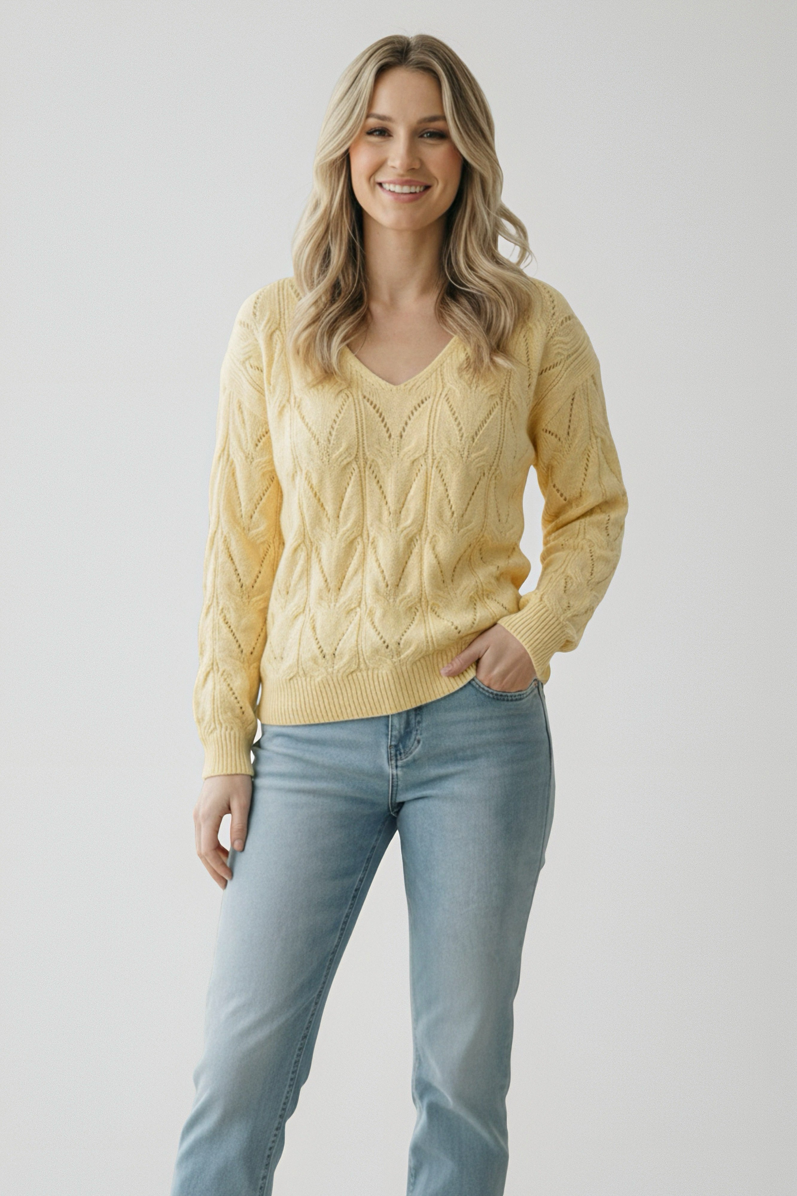 Woman wearing a yellow knit v-neck sweater with a delicate openwork pattern paired with light blue jeans