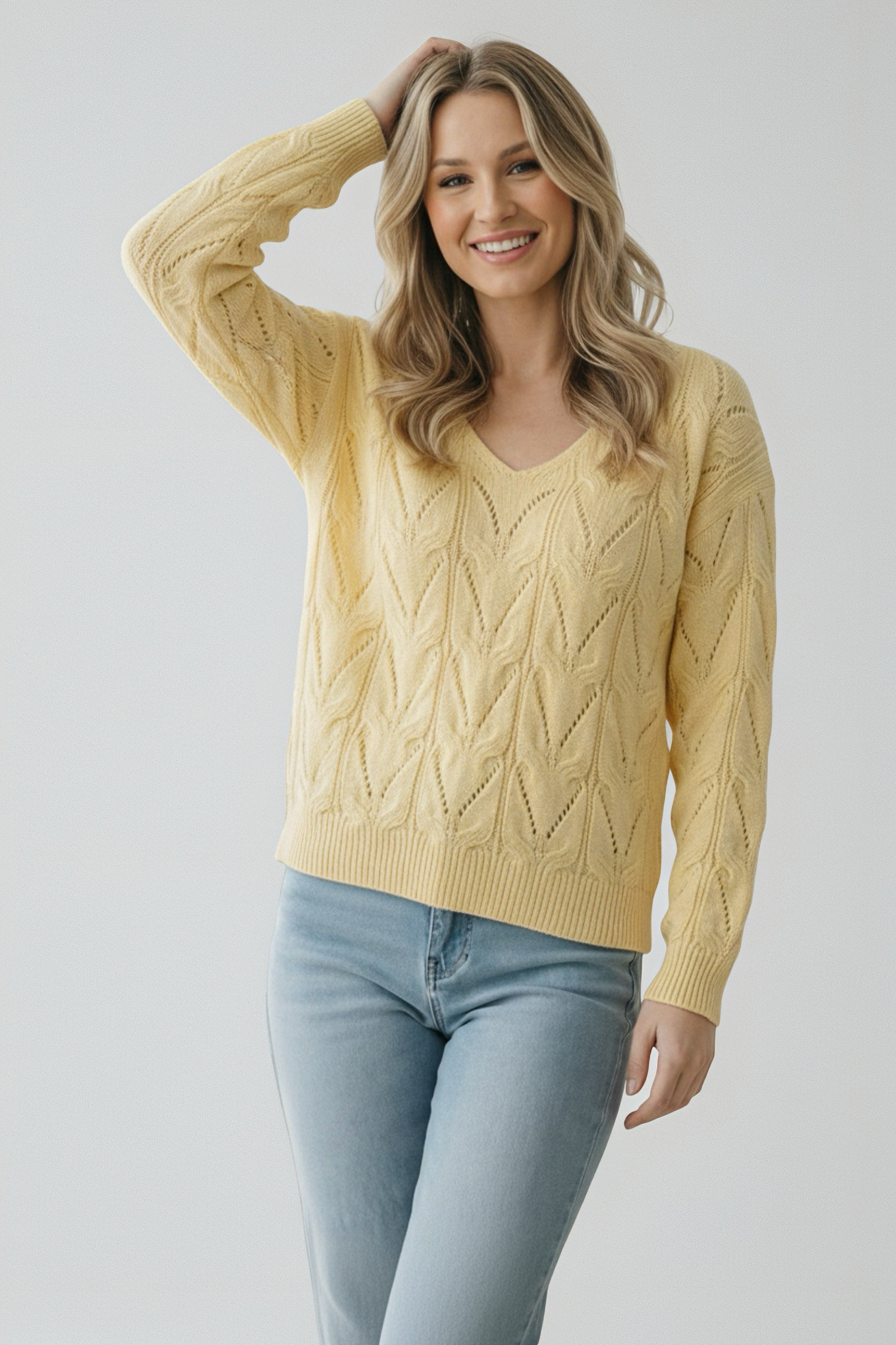 Smiling woman in a soft yellow knit sweater with a delicate chevron pattern paired with light blue jeans
