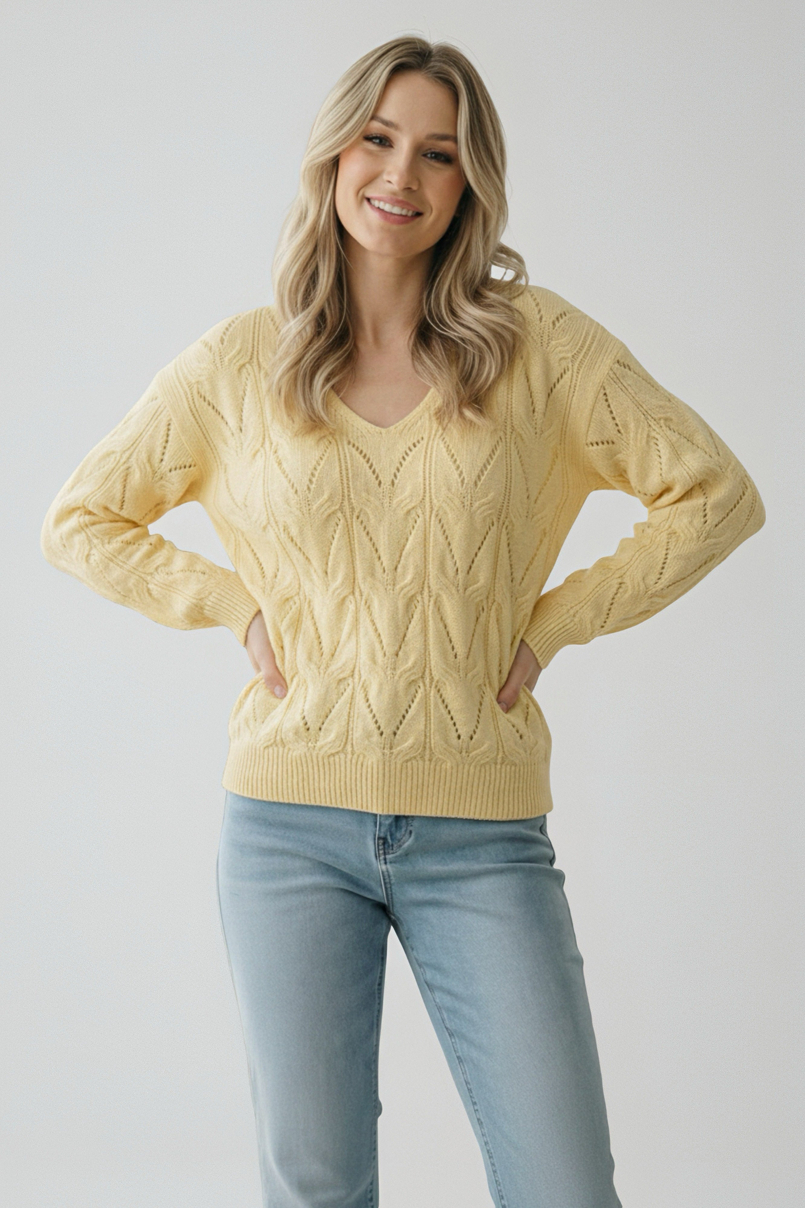 Woman wearing a soft yellow cable knit v-neck sweater paired with light blue jeans standing with hands on hips