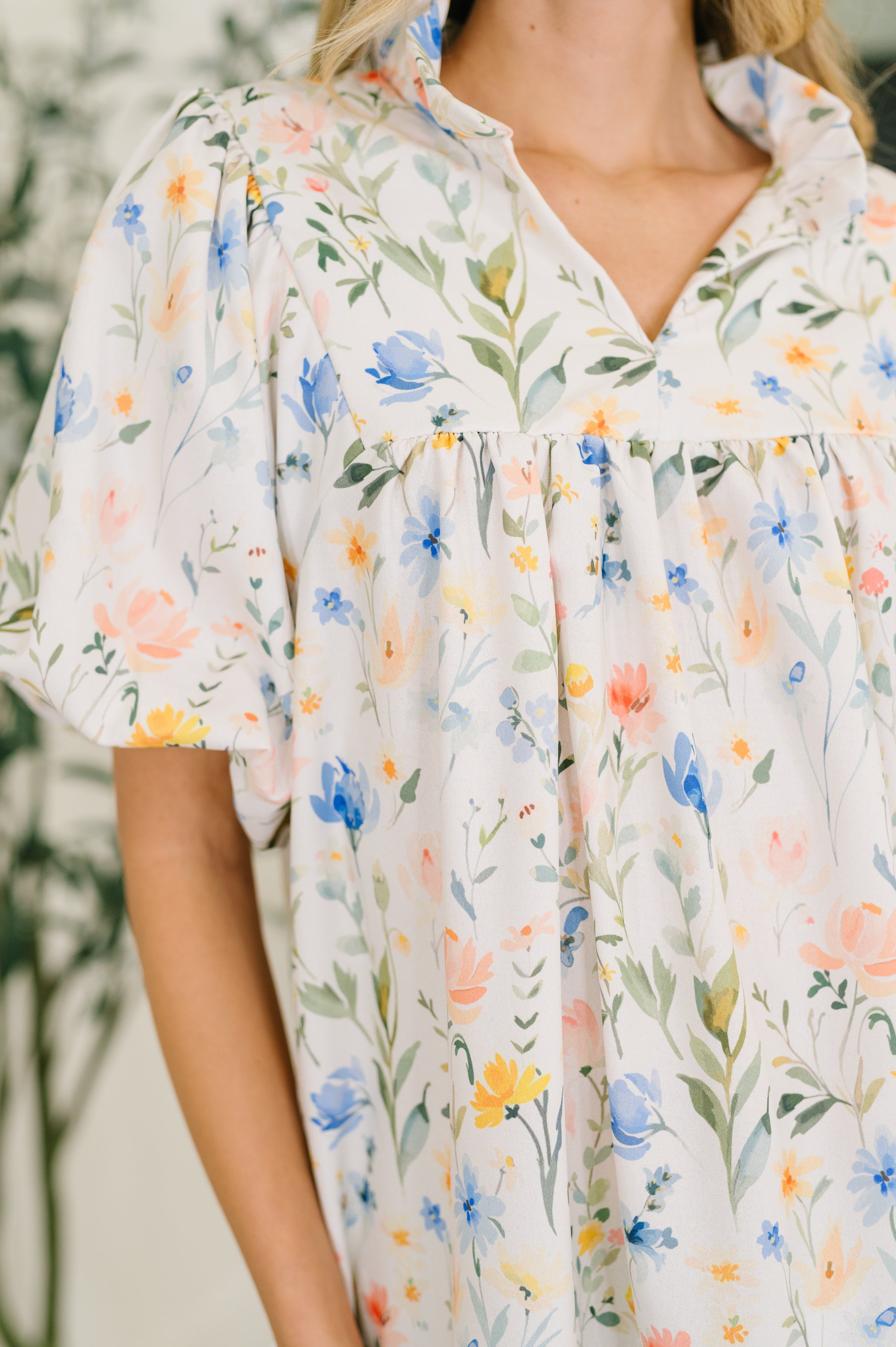 Close-up of cream floral blouse with notch neck, ruffled collar, and puffed sleeves in bright eclectic setting