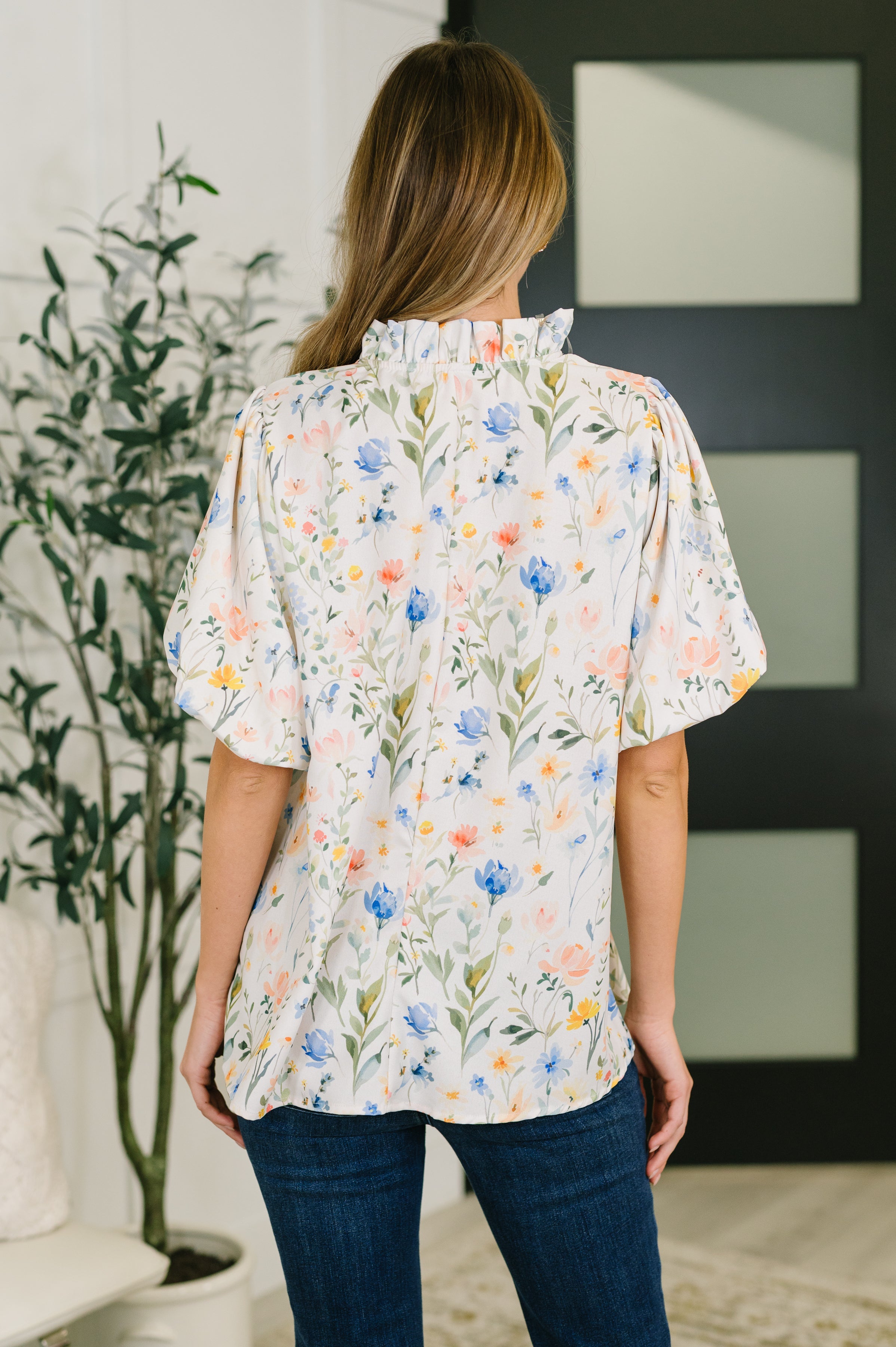 Woman wearing a cream floral blouse with ruffled notch neck and puff sleeves paired with dark jeans in eclectic space