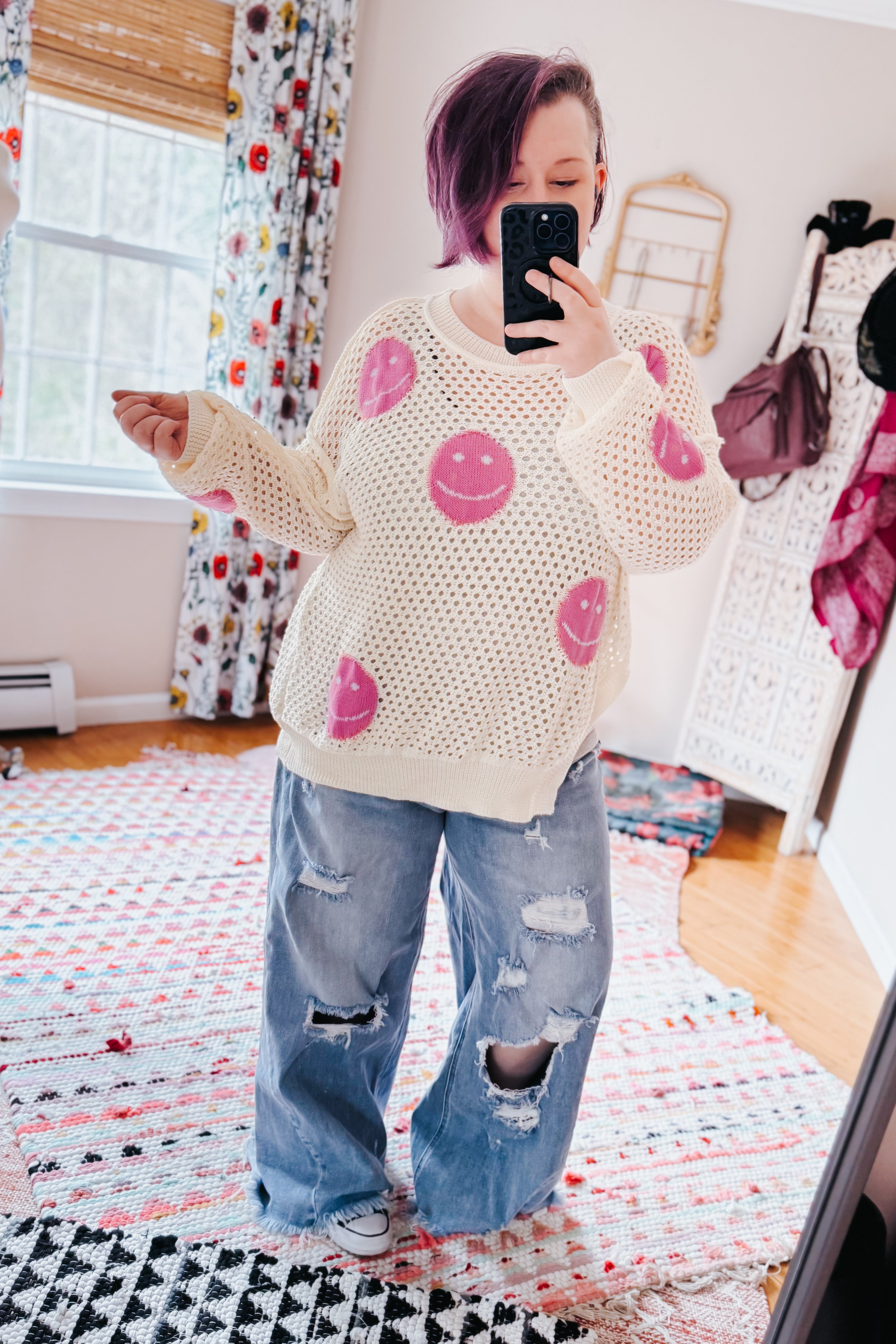 Woman taking mirror selfie wearing beige and pink In My Feelings Smiley Open Knit Top with loose distressed jeans in colorful room