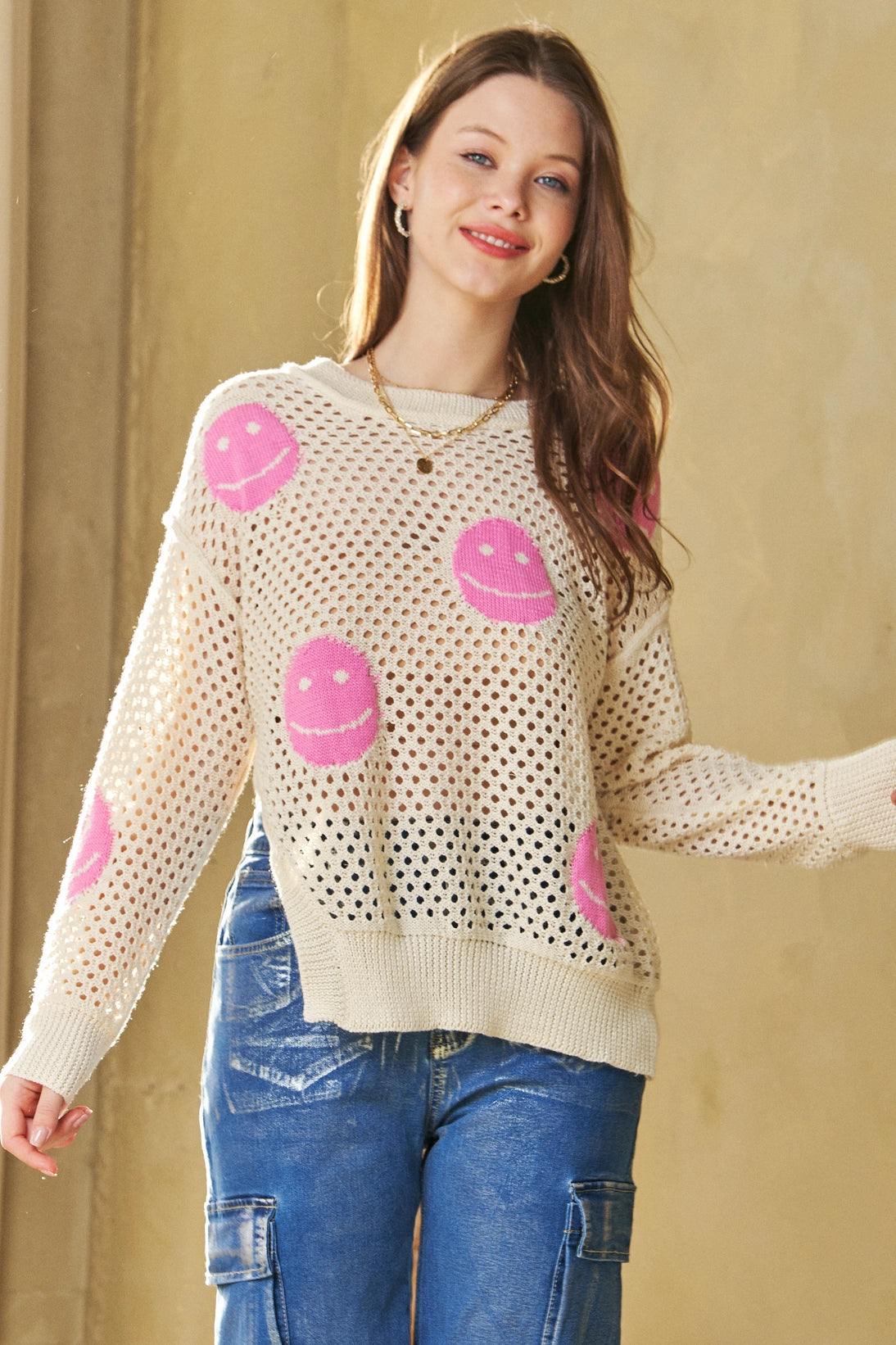 Woman wearing beige and pink In My Feelings Smiley Open Knit Top with relaxed fit blue cargo jeans and layered necklaces indoors