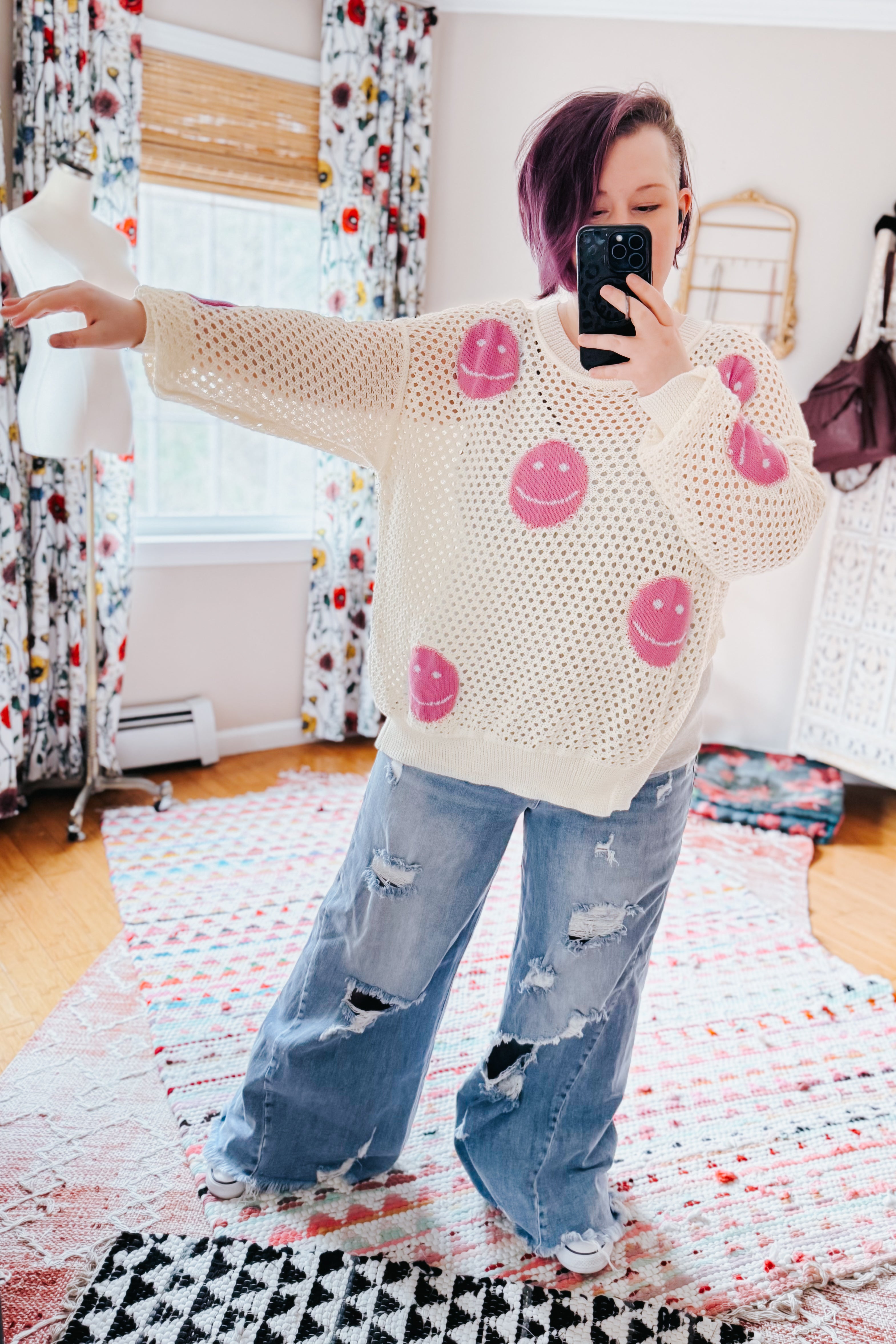 Woman taking mirror selfie wearing beige and pink In My Feelings Smiley Open Knit Top with ripped wide-leg jeans in bright room