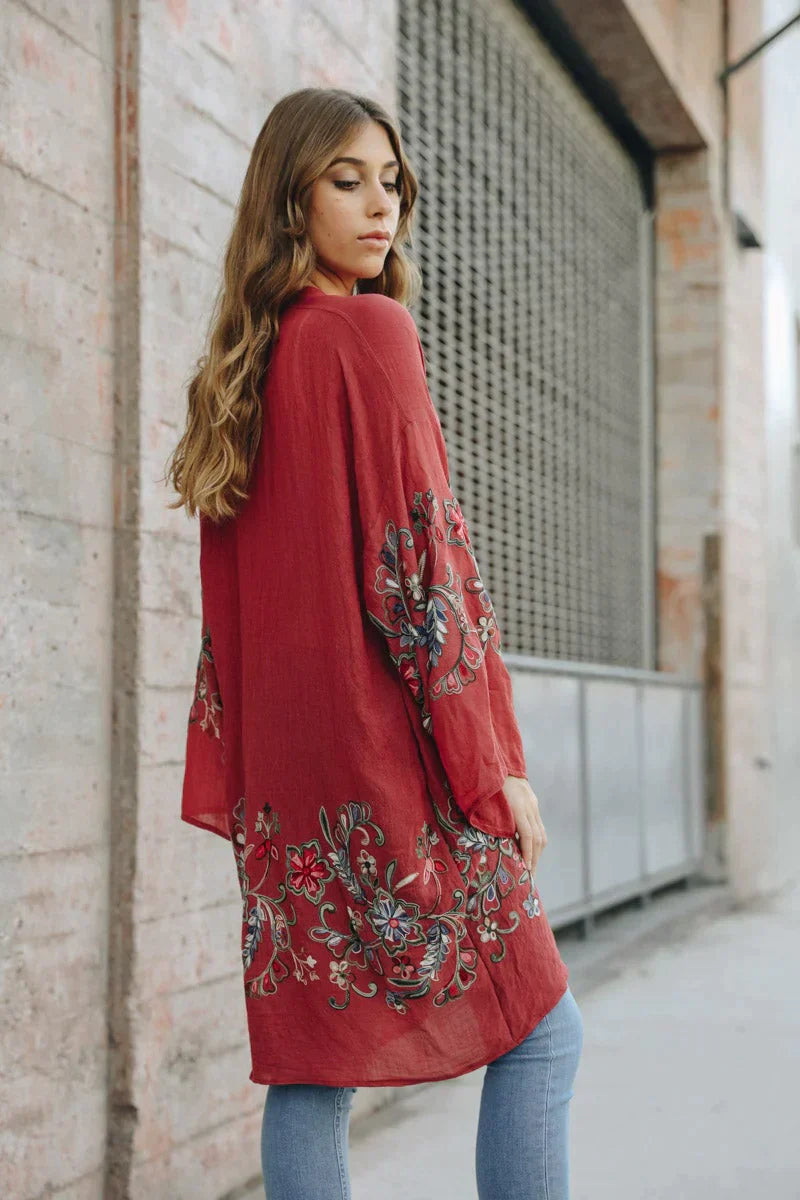 Woman wearing crimson In The Meadow embroidered duster with floral details over light wash jeans standing outdoors