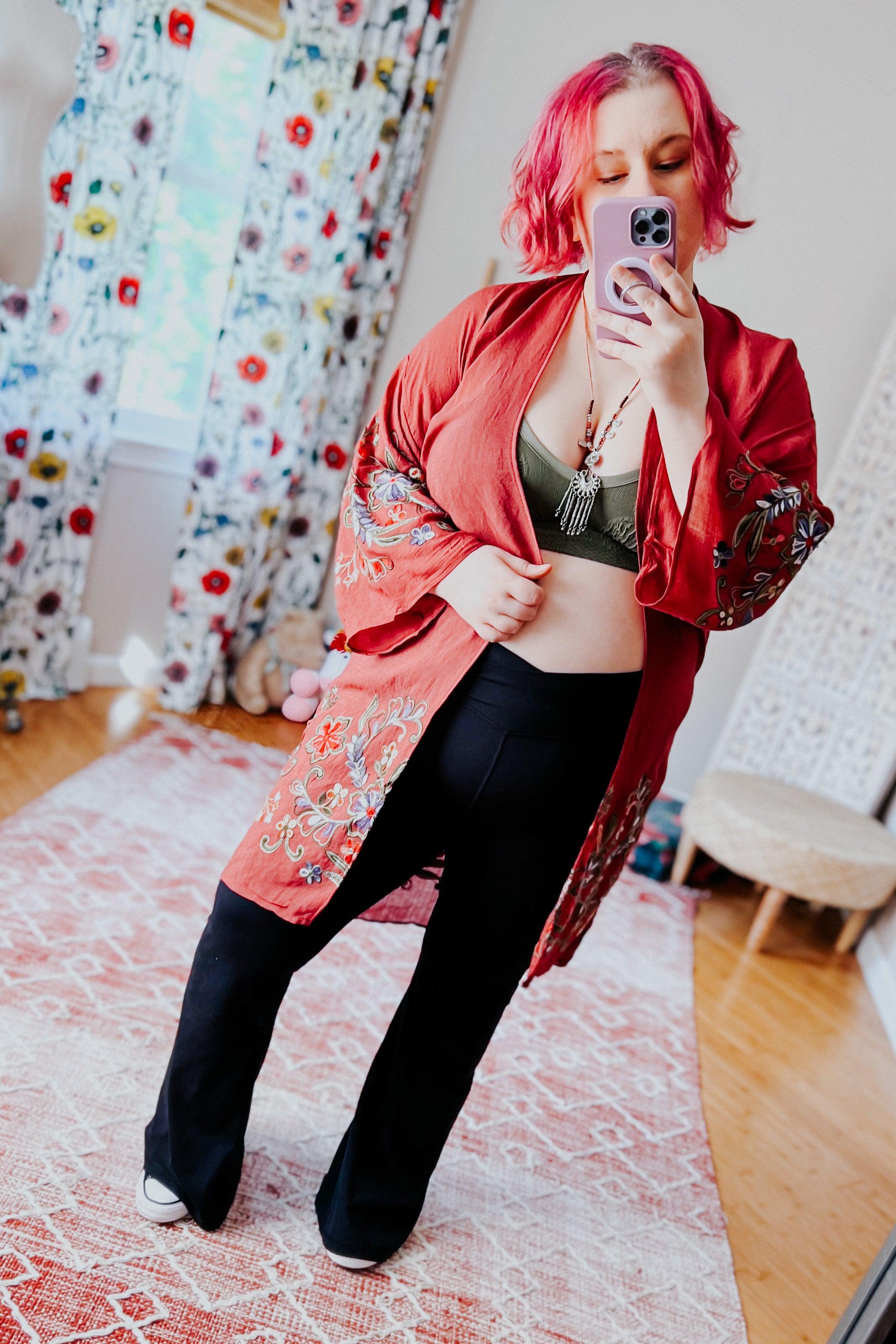 Woman taking mirror selfie wearing crimson In The Meadow embroidered duster paired with black pants and olive cropped top indoors