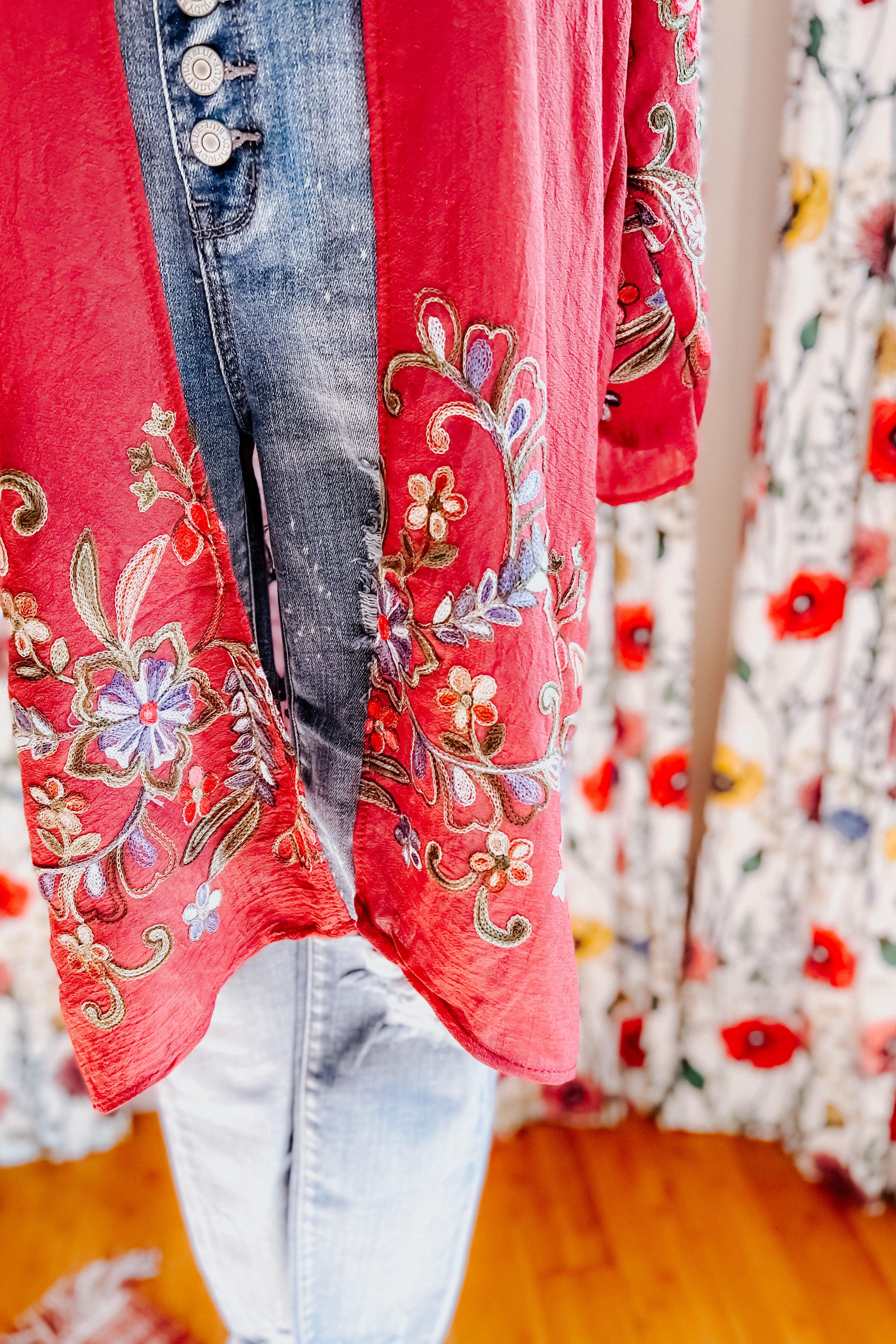 Close-up of crimson In The Meadow embroidered duster hem with floral motifs layered over faded blue jeans