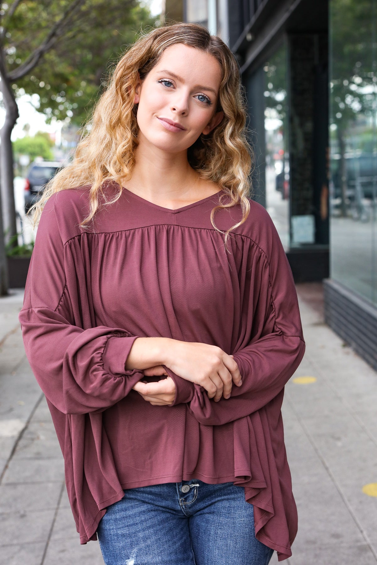 Woman outdoors wearing wine In This Groove modal knit top with loose gathered sleeves and relaxed fit paired with blue jeans