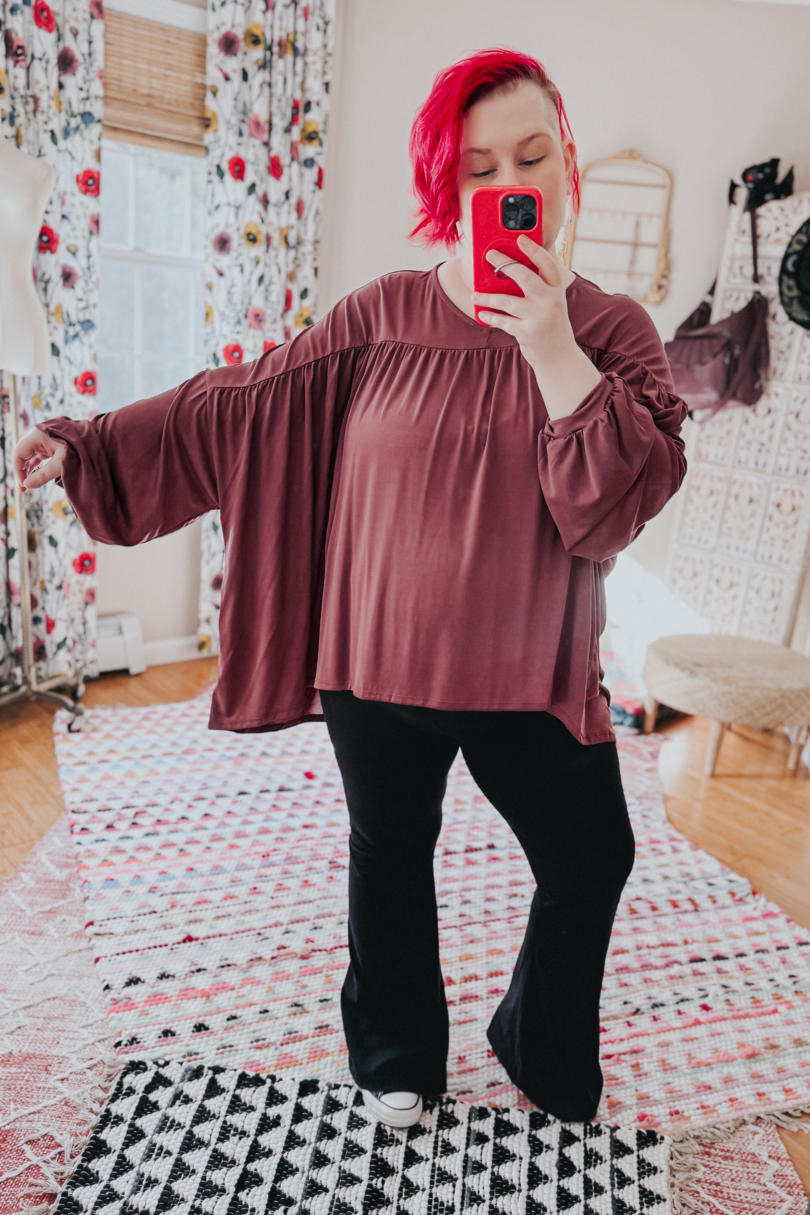 Plus-size woman taking selfie wearing wine In This Groove modal knit top with loose sleeves and black pants indoors