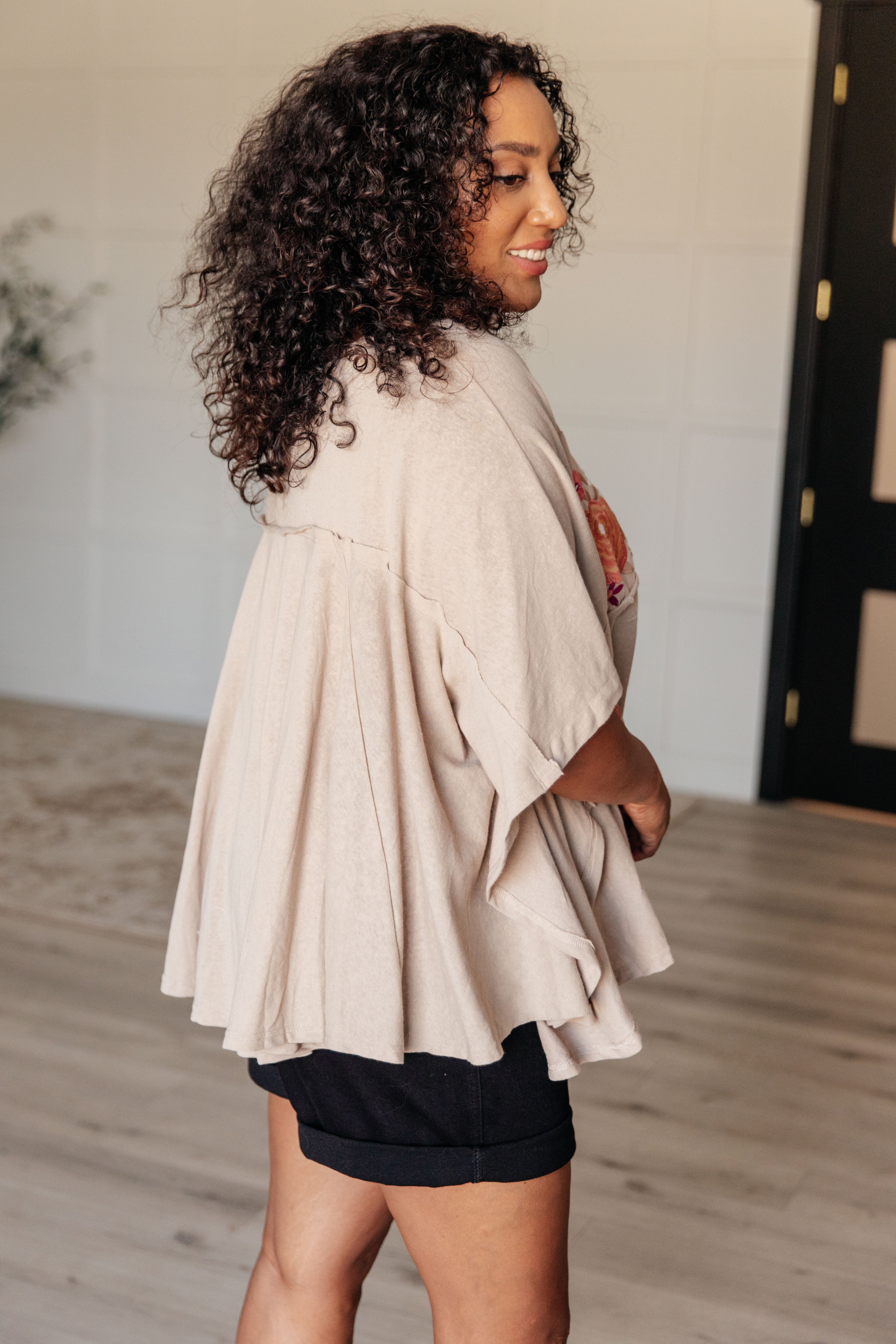 Woman with curly hair wearing loose mocha Isabel tunic featuring flowing back pleats and short sleeves in bright room