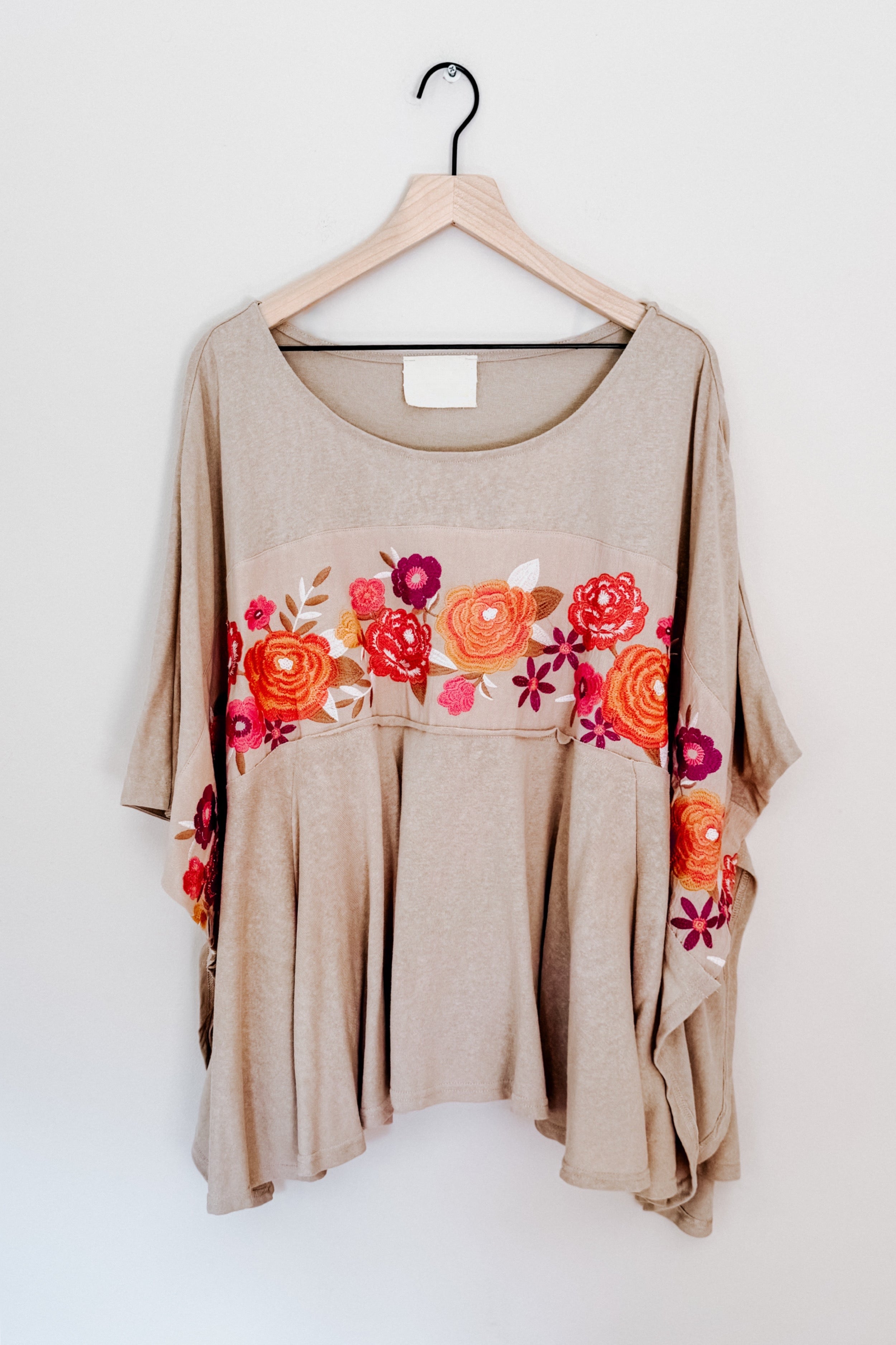 Mocha Isabel tunic with embroidered floral band in warm tones and flowy silhouette hanging on wooden hanger against white wall