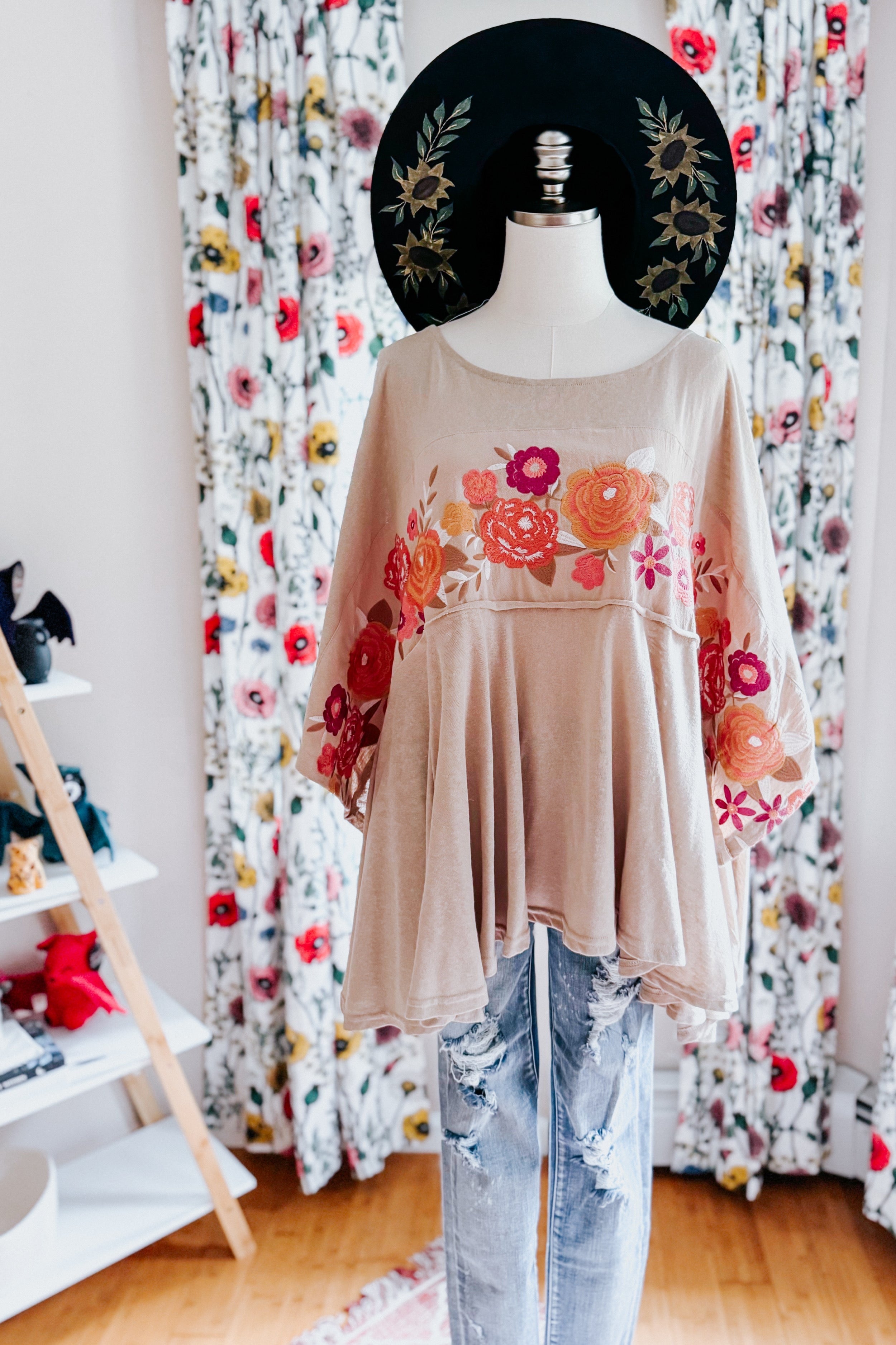 Mocha Isabel embroidered tunic with floral design in warm tones displayed on mannequin with distressed light blue jeans