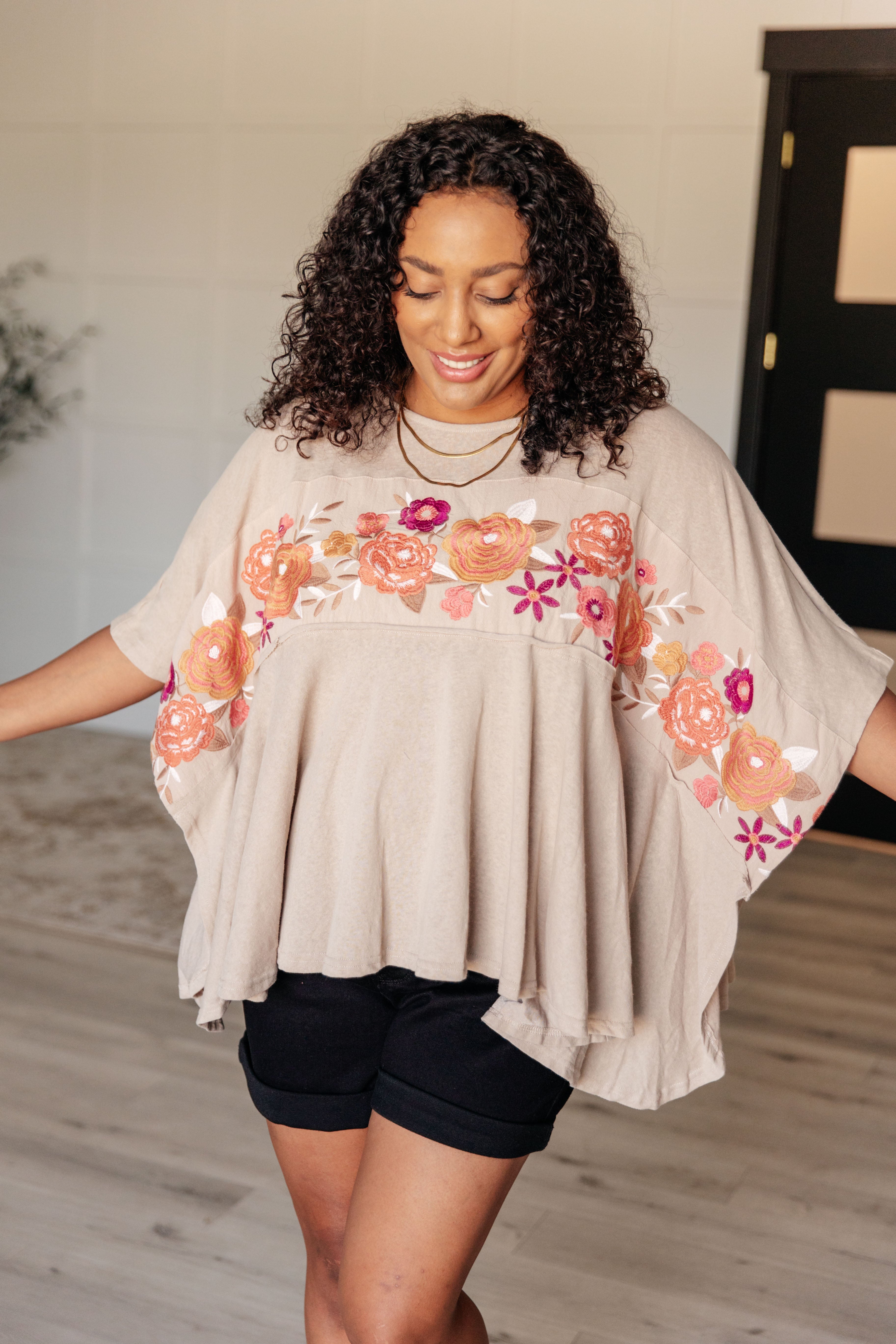 Woman wearing mocha Isabel tunic with embroidered floral band and draped flowy silhouette indoors